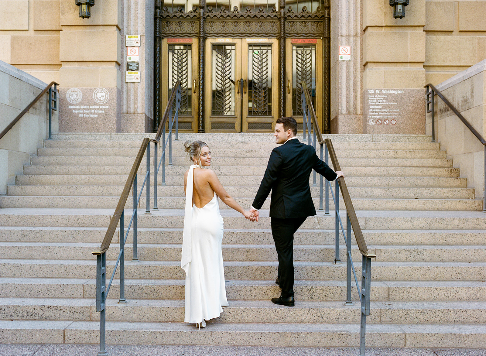 Bride and groom holding hands while walking up the steps of Phoenix City Hall during their courthouse wedding