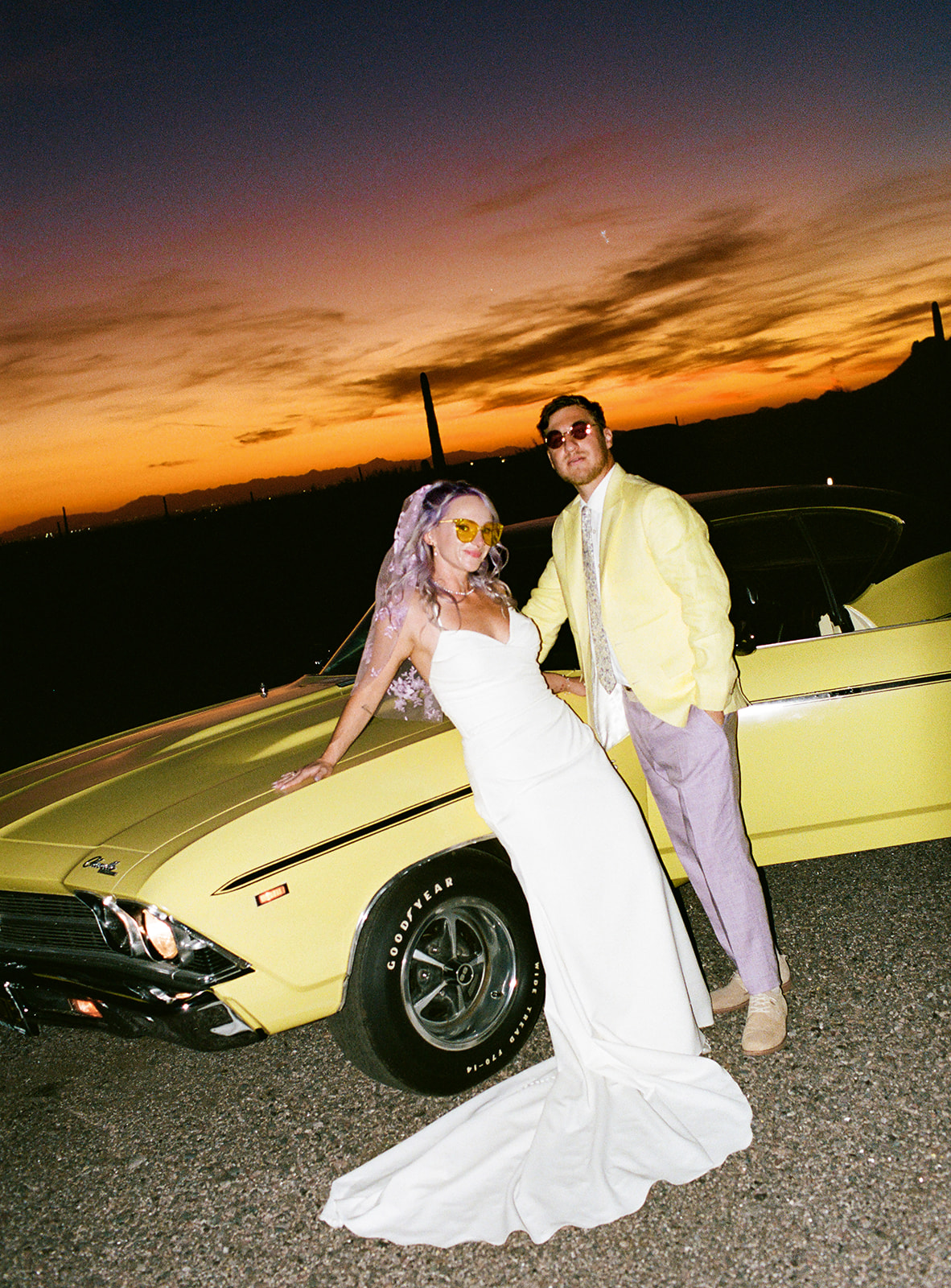 Bride and groom posing together in front of a vintage car at sunset in the Arizona desert