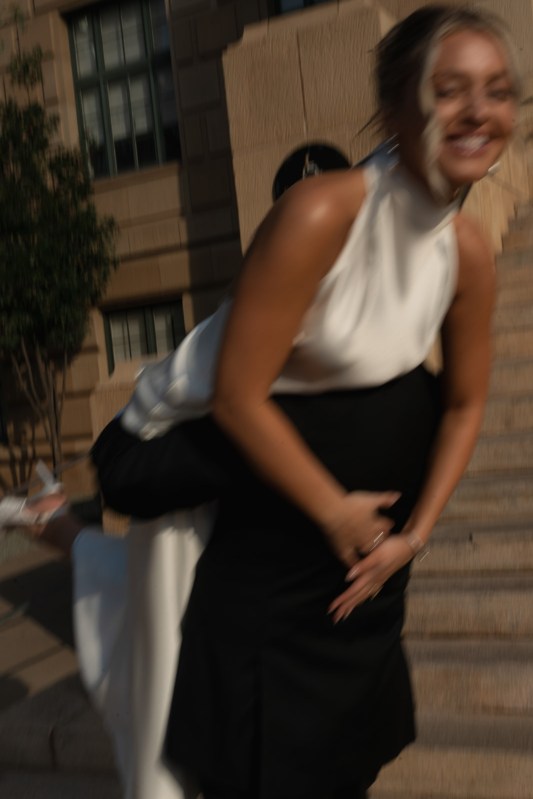Playful candid moment of bride laughing while being lifted during wedding photos outside a courthouse