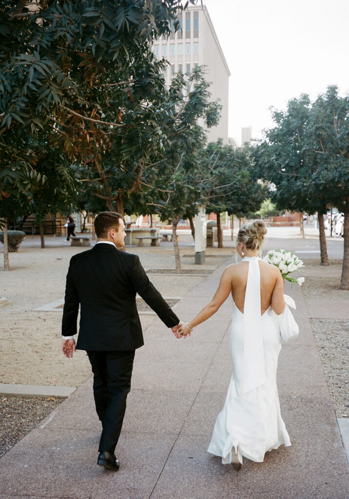 Bride and groom walking hand in hand through downtown Phoenix after their courthouse wedding, bride holding a bouquet of white tulips