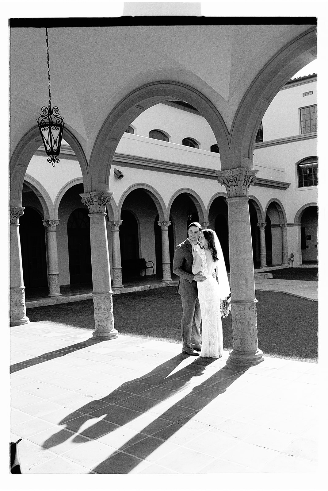 Couple embracing in sunlit courtyard with arches