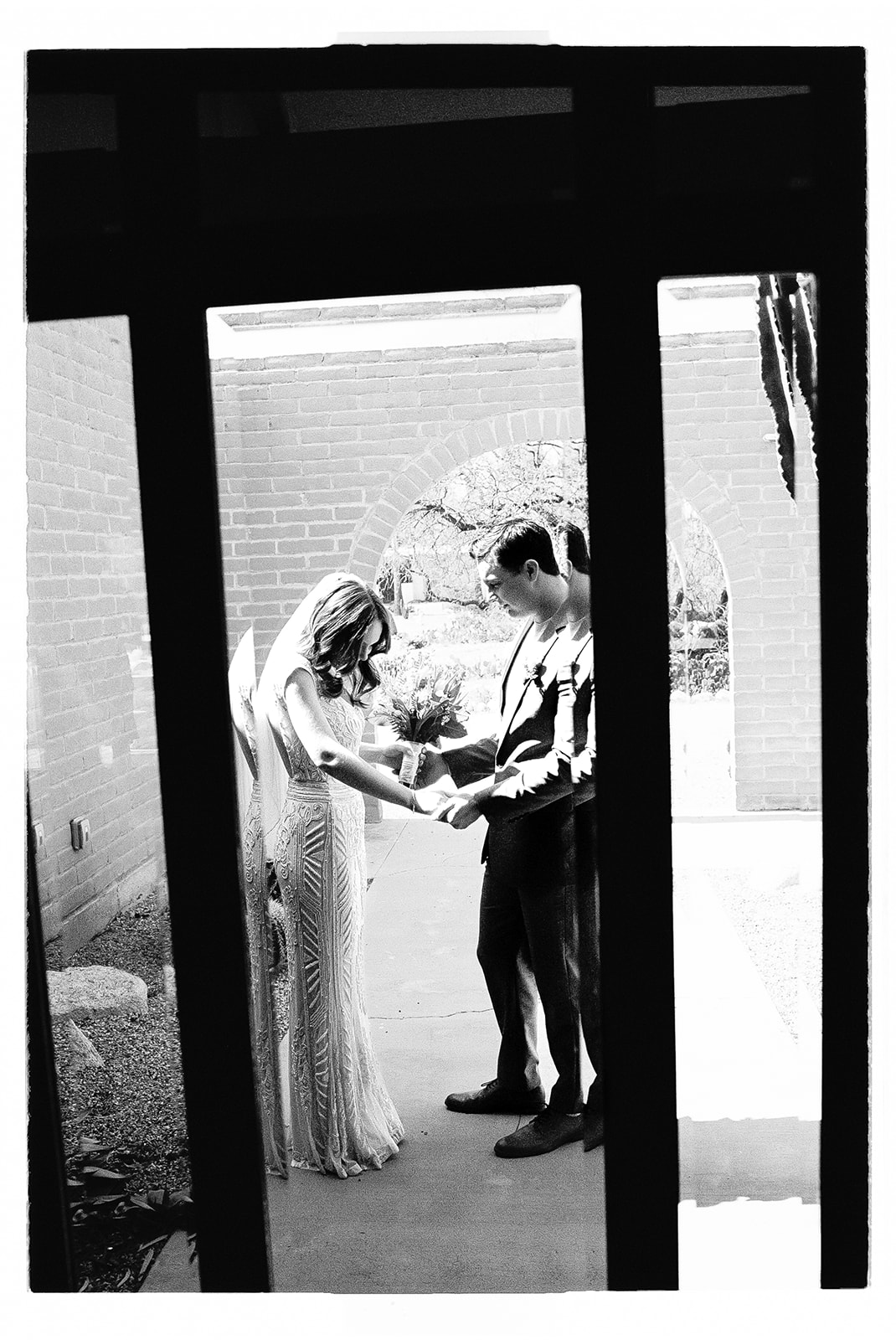 Black-and-white photo of couple holding hands through window reflection
