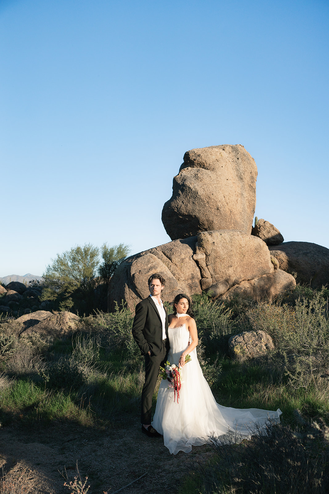 Bride and groom posing near large rock formation
