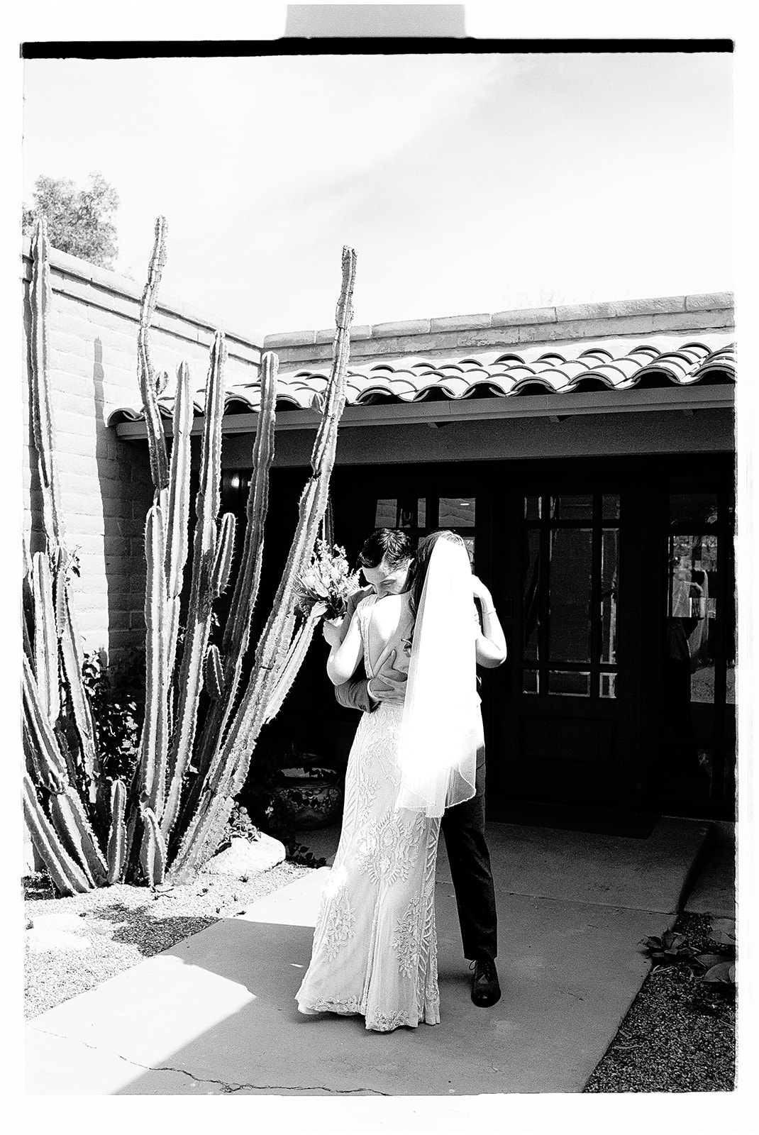 Non-traditional wedding couple embracing outside rustic building