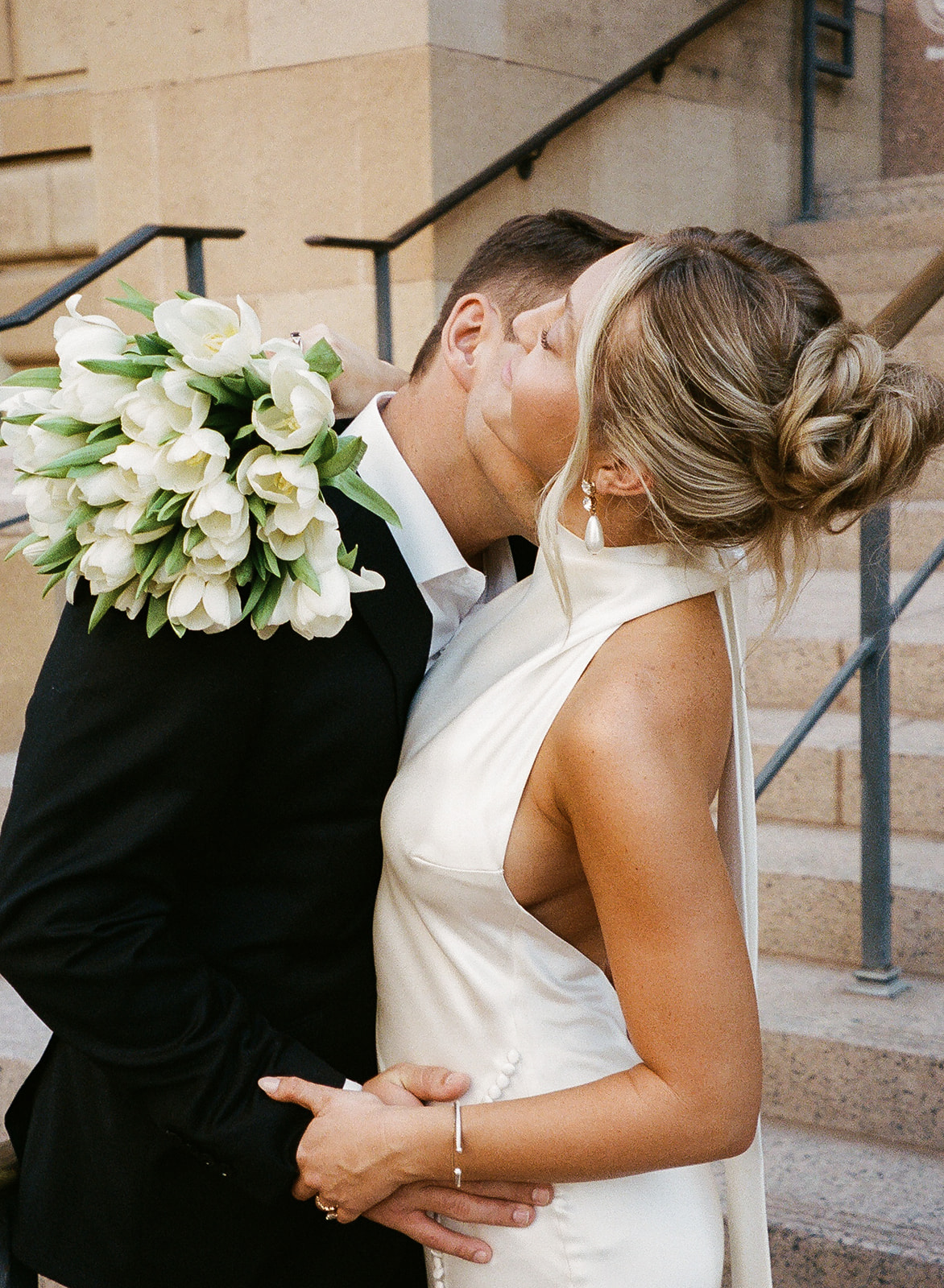 Couple kissing, bride holding bouquet on steps