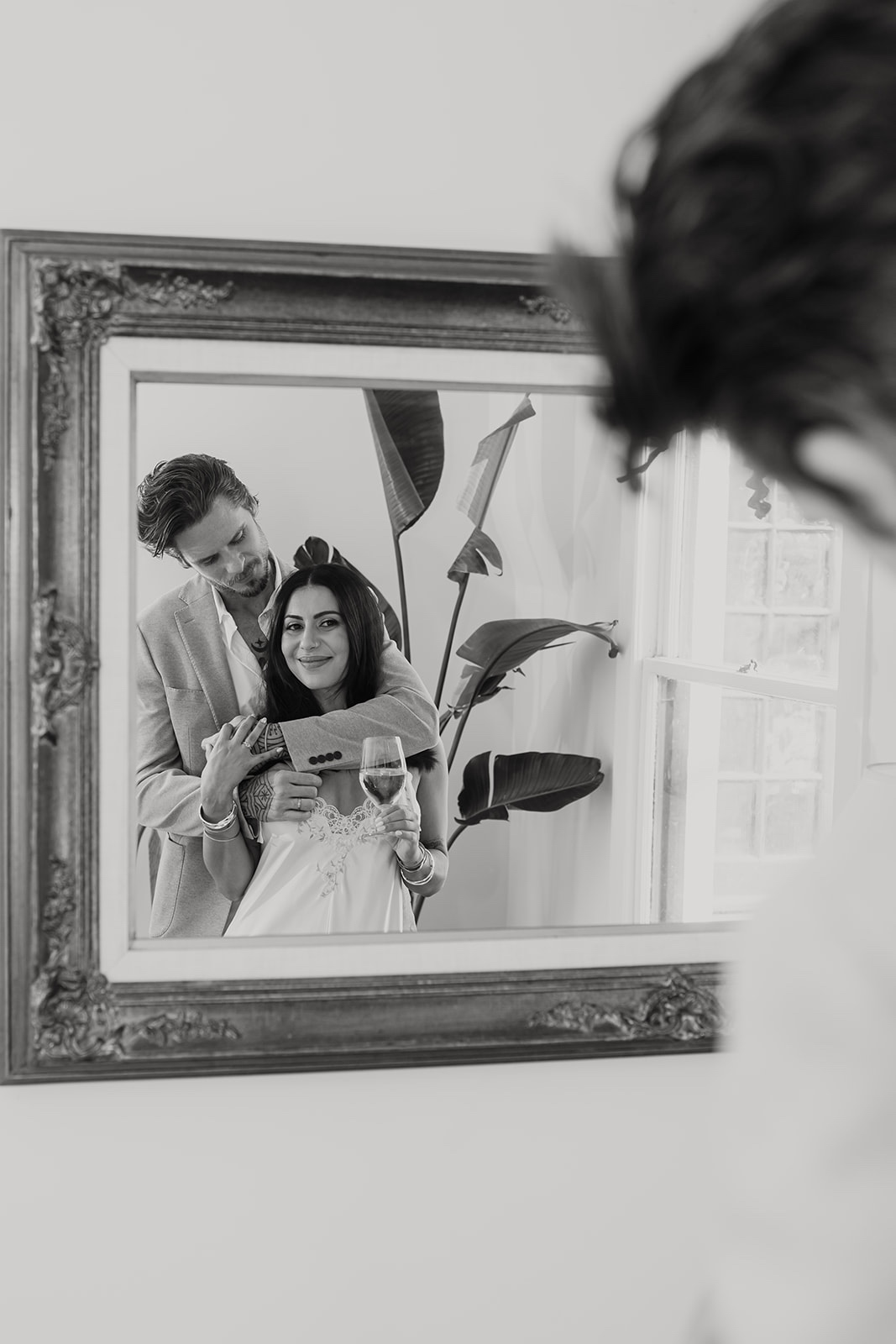 Black-and-white photo of couple indoors looking in mirror