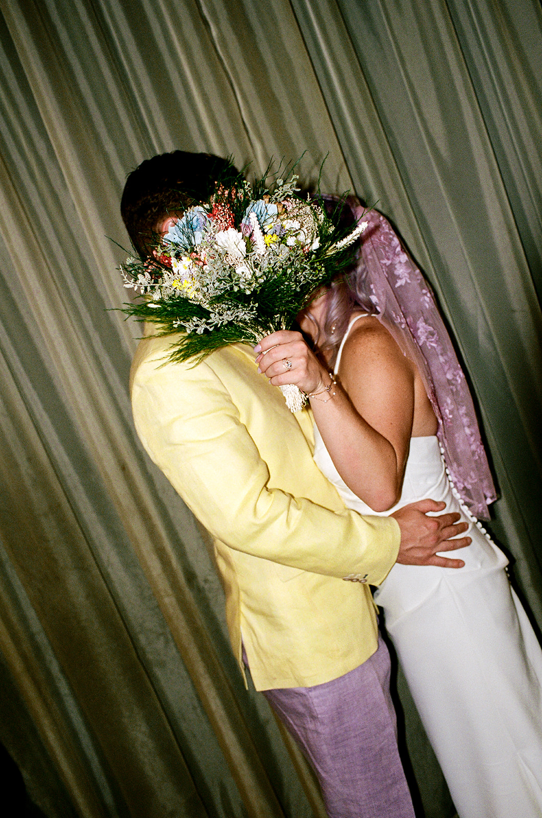 Couple embracing, bride holding bouquet over face
