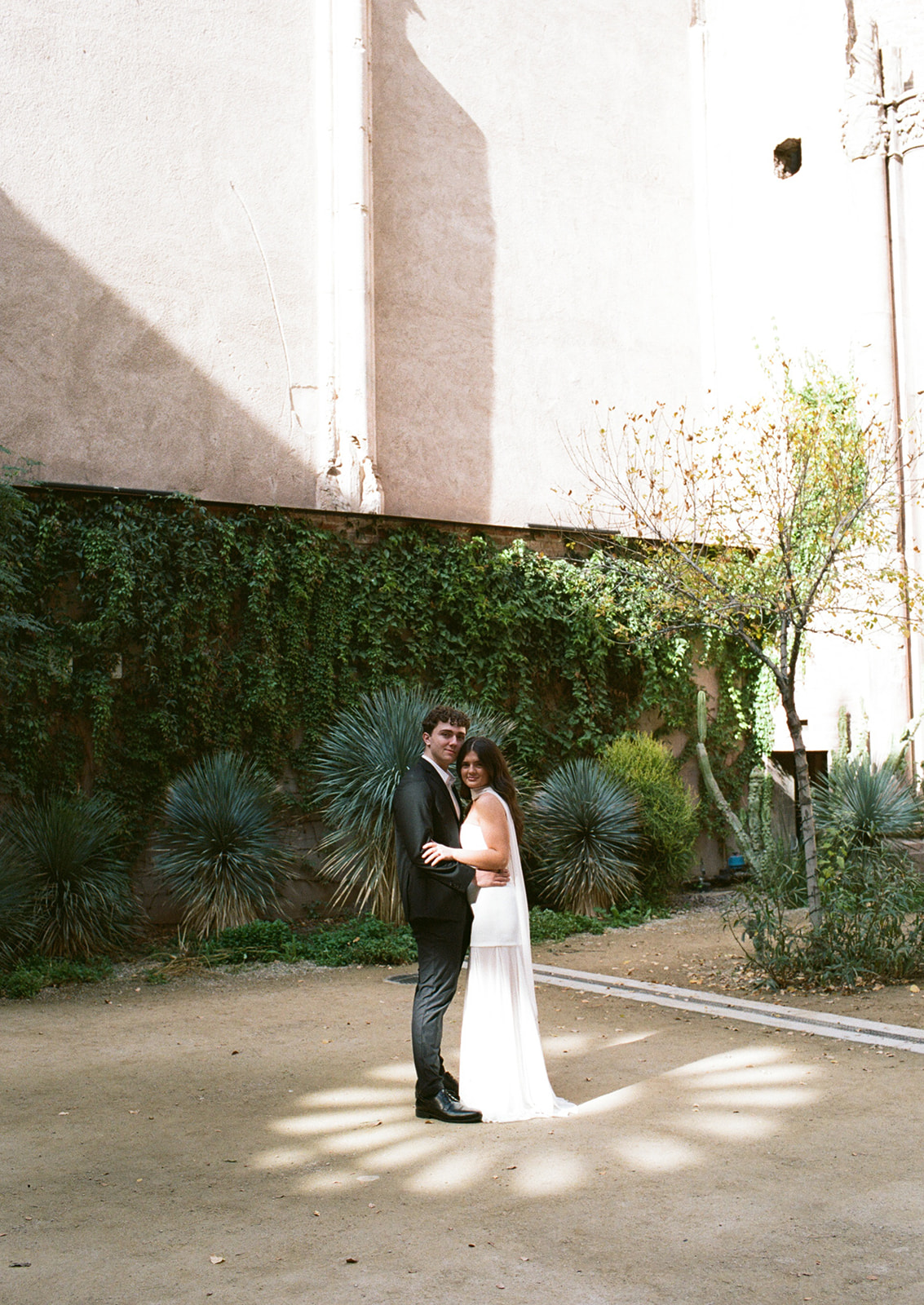 Couple standing together in a sunlit courtyard surrounded by greenery at unique wedding venues in Phoenix Arizona— The Abbey at Monroe