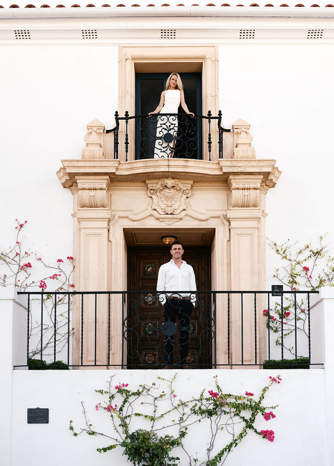Bride standing on balcony above groom at Wrigley Mansion wedding venue in Scottsdale Arizona with Spanish-style architecture and white exterior