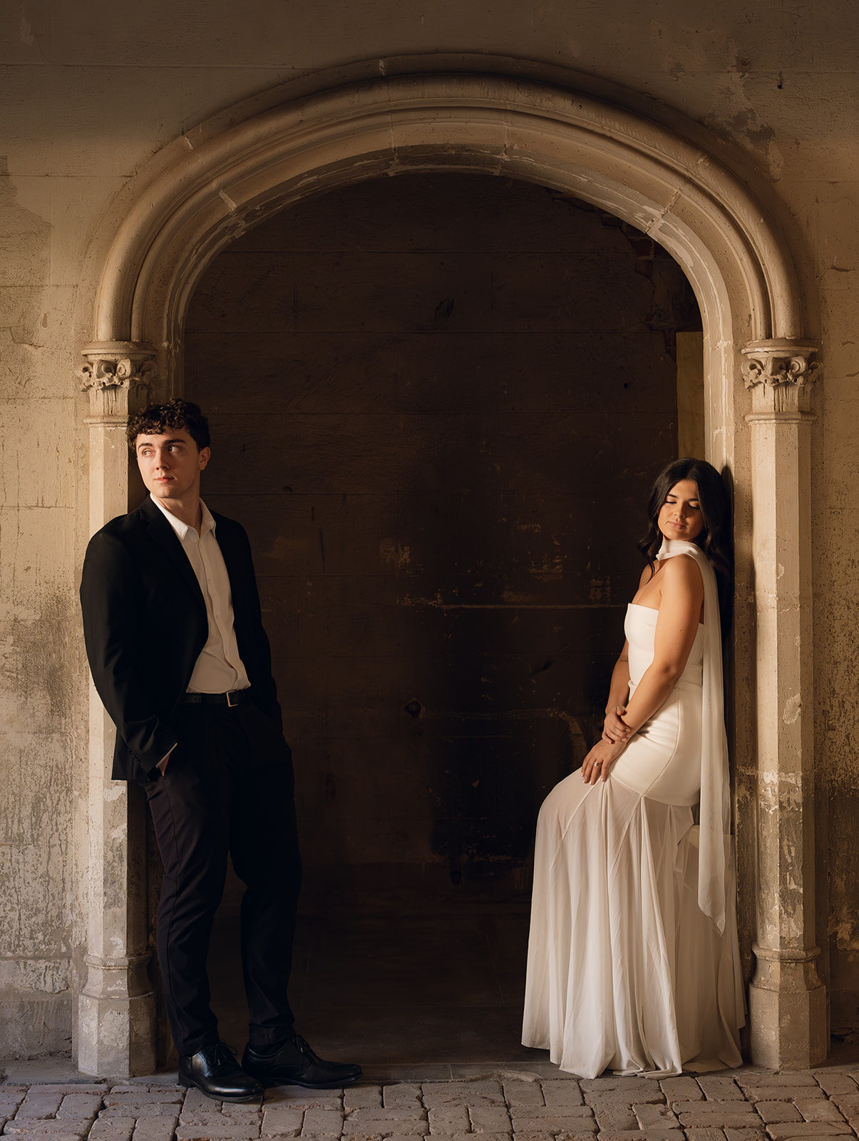 Bride and groom posing separately under a stone archway, looking in opposite directions in a historic wedding venues in Phoenix Arizona— The Abbey on Monroe
