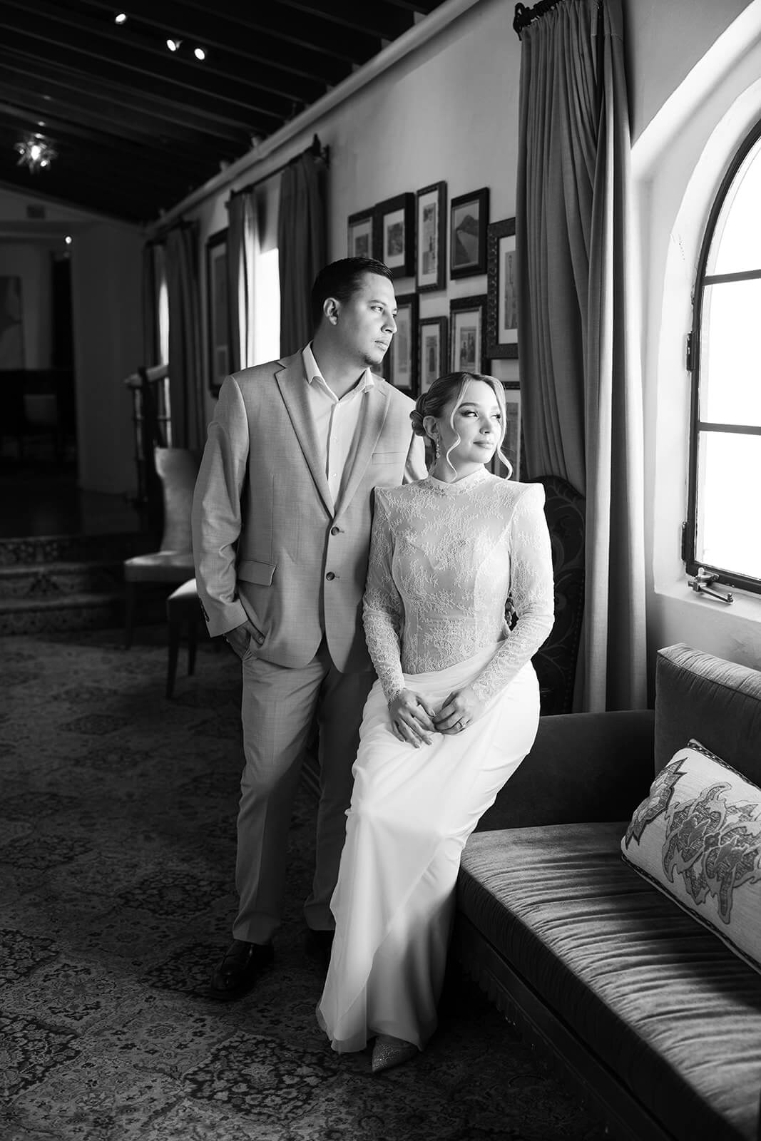 Black and white image of couple by a window inside a cozy micro wedding venue, with soft natural light highlighting their quiet moment.
