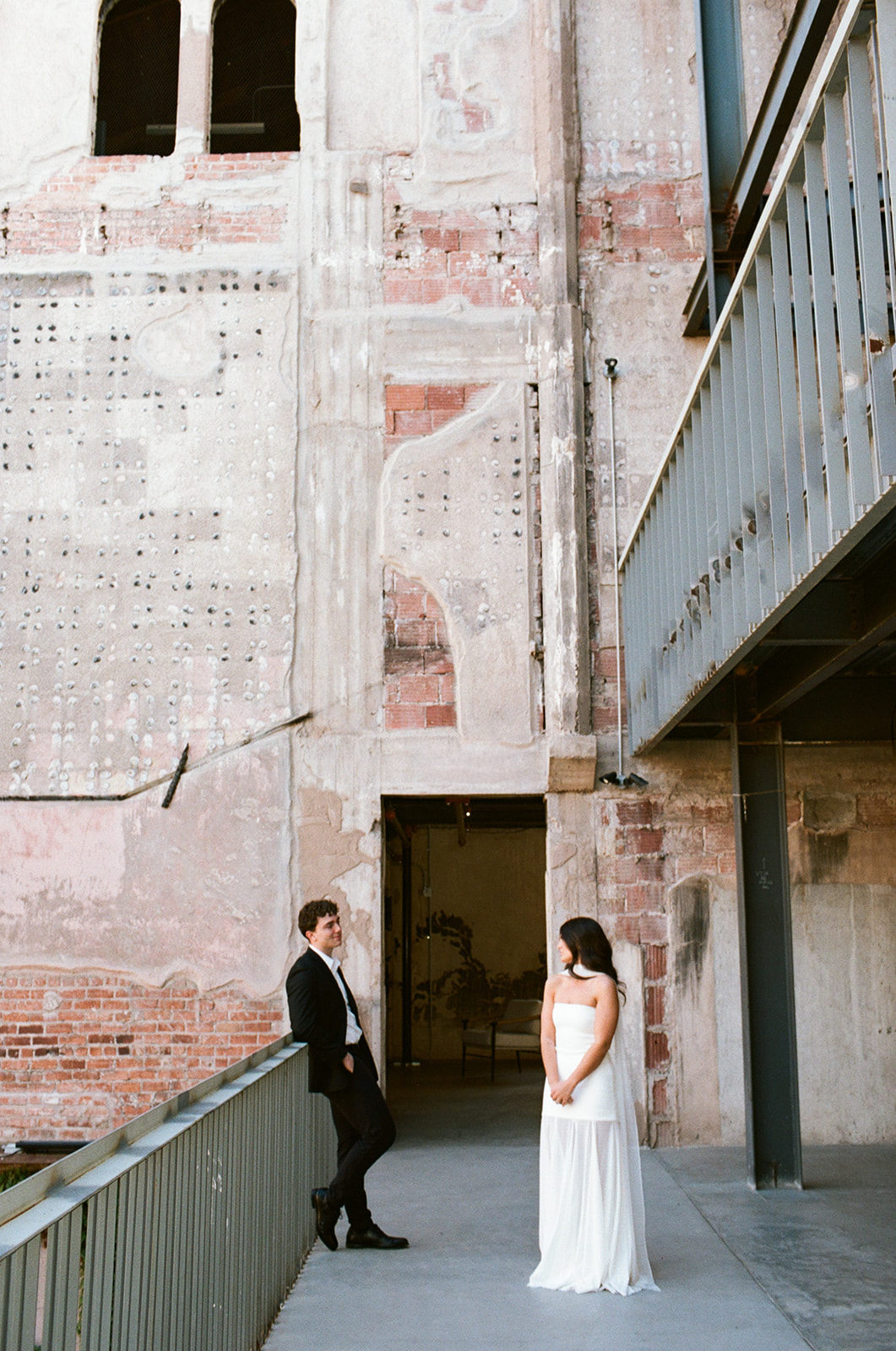 Bride and groom standing apart and looking at each other on an industrial balcony walkway with exposed brick and historic textures at outdoor wedding venues in phoenix — The Abbey on Monroe