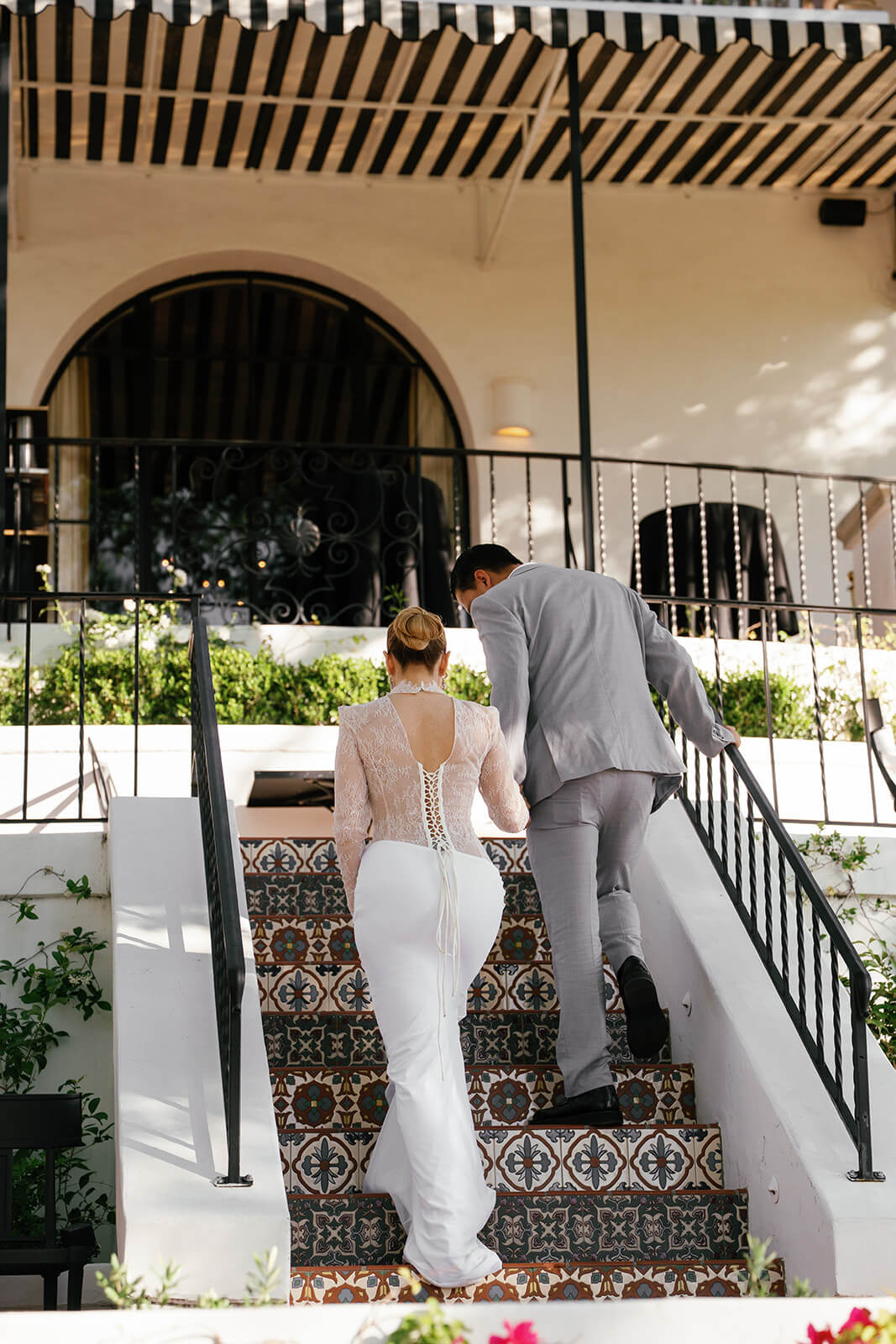 Bride and groom walking up patterned tile stairs at the Wrigley Mansion, a luxury Phoenix Arizona wedding venue with Spanish-style architecture and striped awnings.
