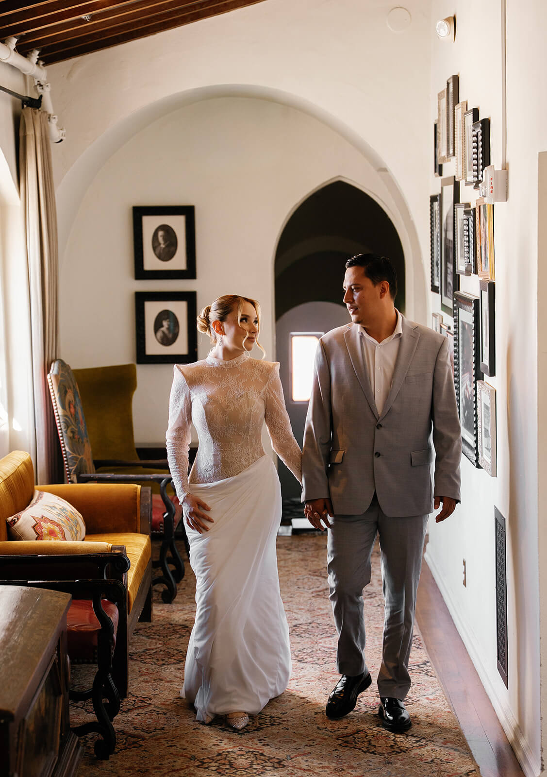 Bride and groom walking hand in hand down a curved hallway with patterned carpet inside the Wrigley Mansion, a unique Arizona wedding venue.
