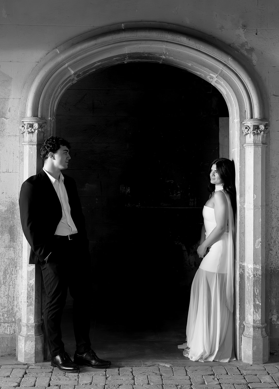 Black and white photo of bride and groom standing apart and facing each other beneath a stone archway inside a historic wedding venue in Phoenix Arizona— The Abbey on Monroe