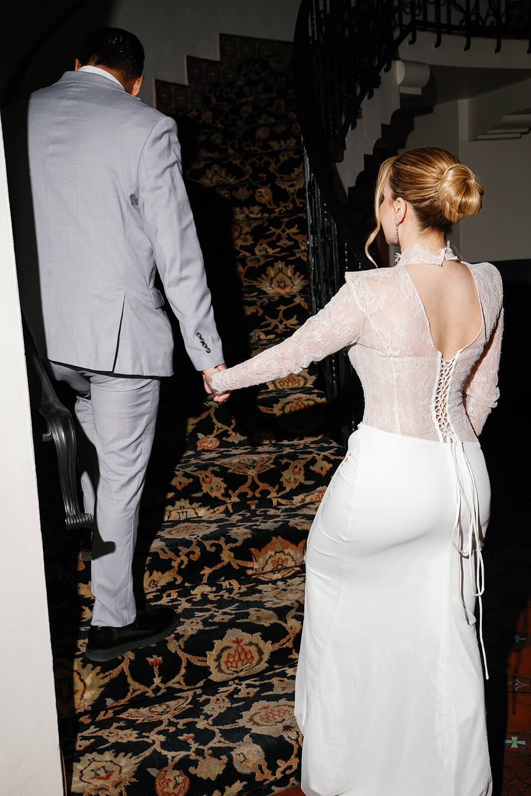 Bride walking up a staircase while holding groom’s hand inside a dramatic micro wedding venue, with patterned flooring and curved iron railings.