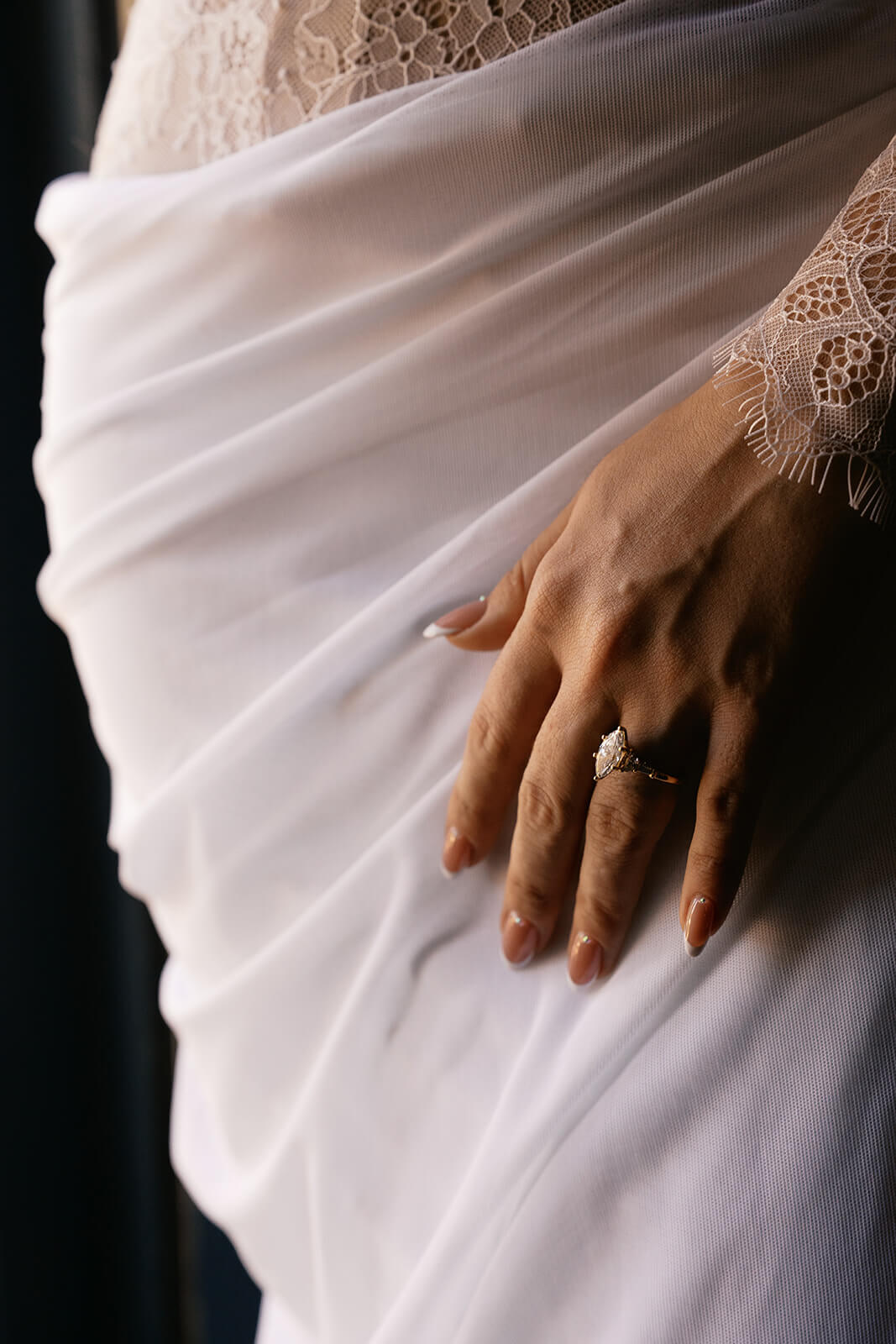 Close-up of bride’s hand resting on her dress, showing an engagement ring and delicate lace sleeve detail during a micro wedding venue bridal portrait.