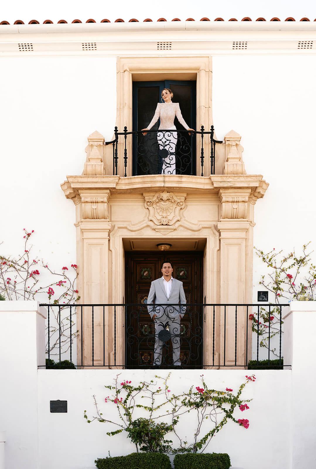 Bride standing alone on a balcony above a grand entrance at a luxury micro wedding venue, framed by classic architecture and soft neutral tones.