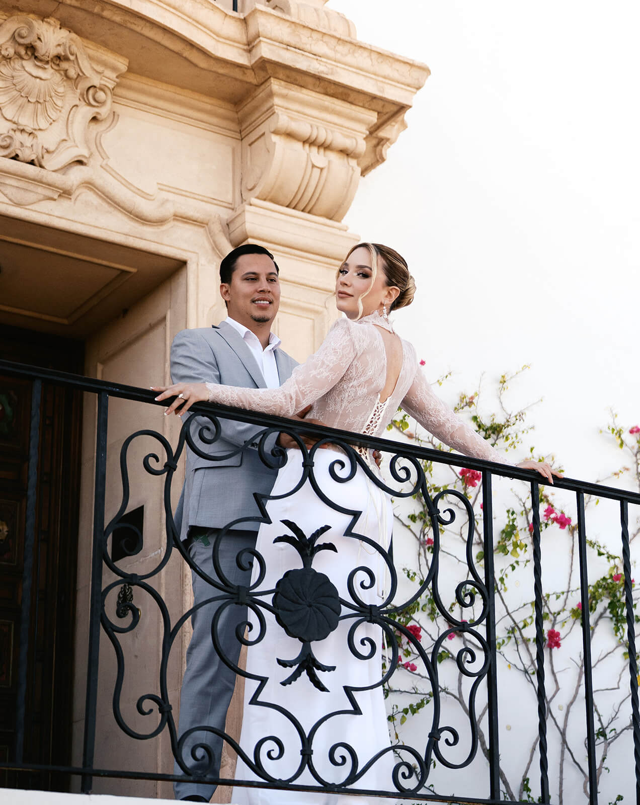 Couple leaning against a balcony railing at a romantic micro wedding venue, with soft light and floral accents creating a timeless feel.