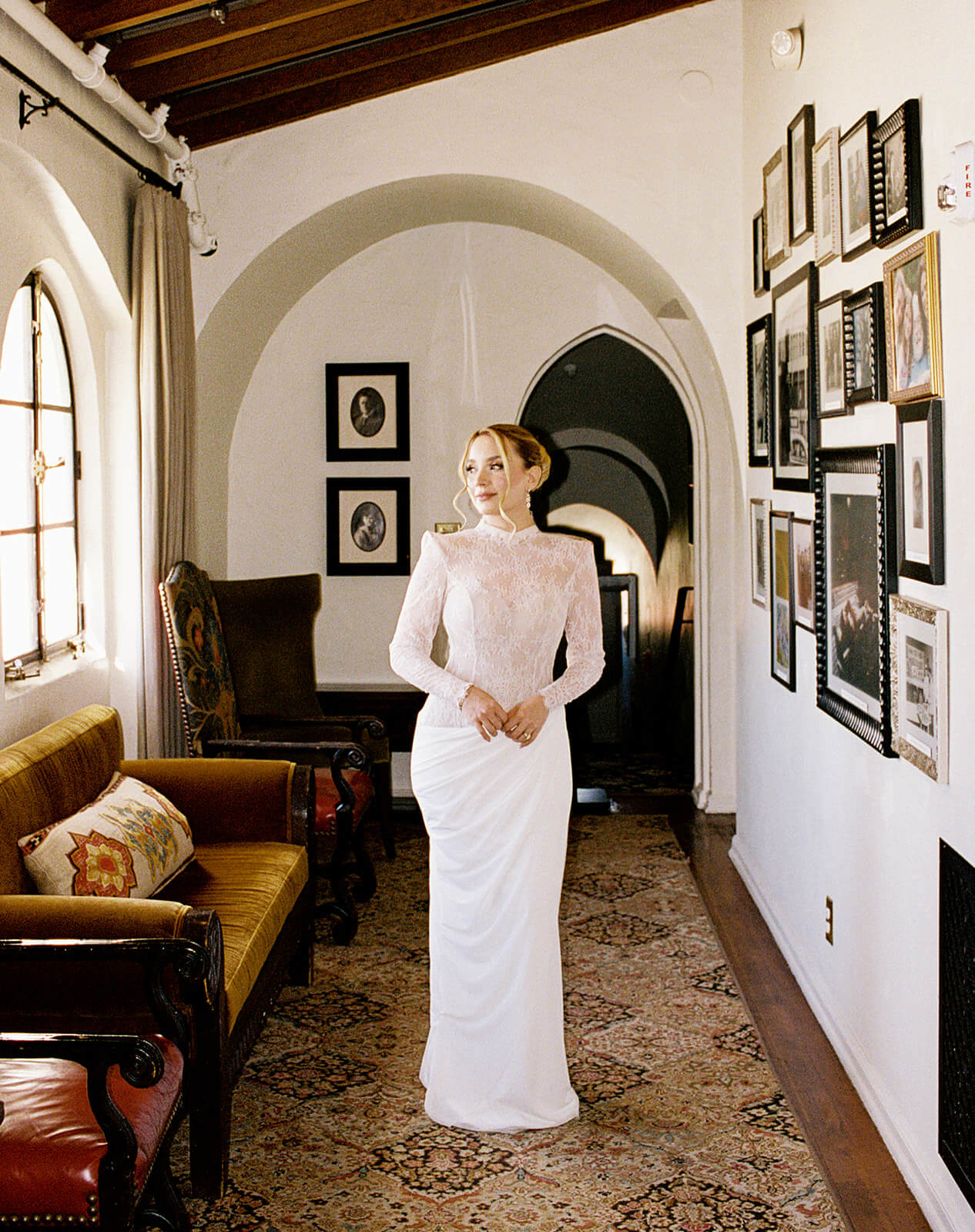 Bride standing in a warm-toned hallway inside a vintage-inspired micro wedding venue, framed by artwork, arched architecture, and textured decor.
