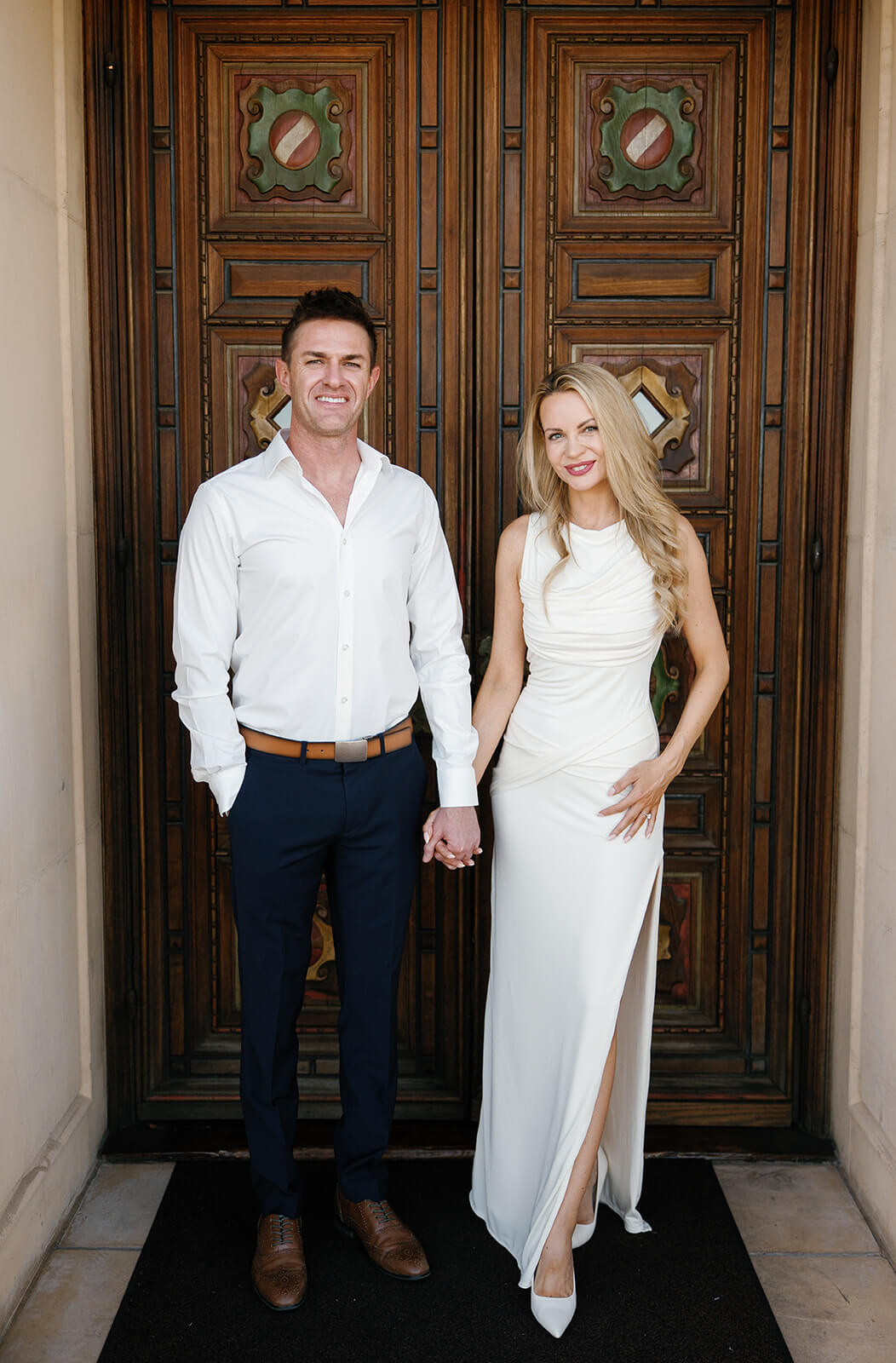 Couple smiling and holding hands in hallway at Wrigley Mansion wedding venue in Phoenix Arizona with framed gallery wall and warm natural light