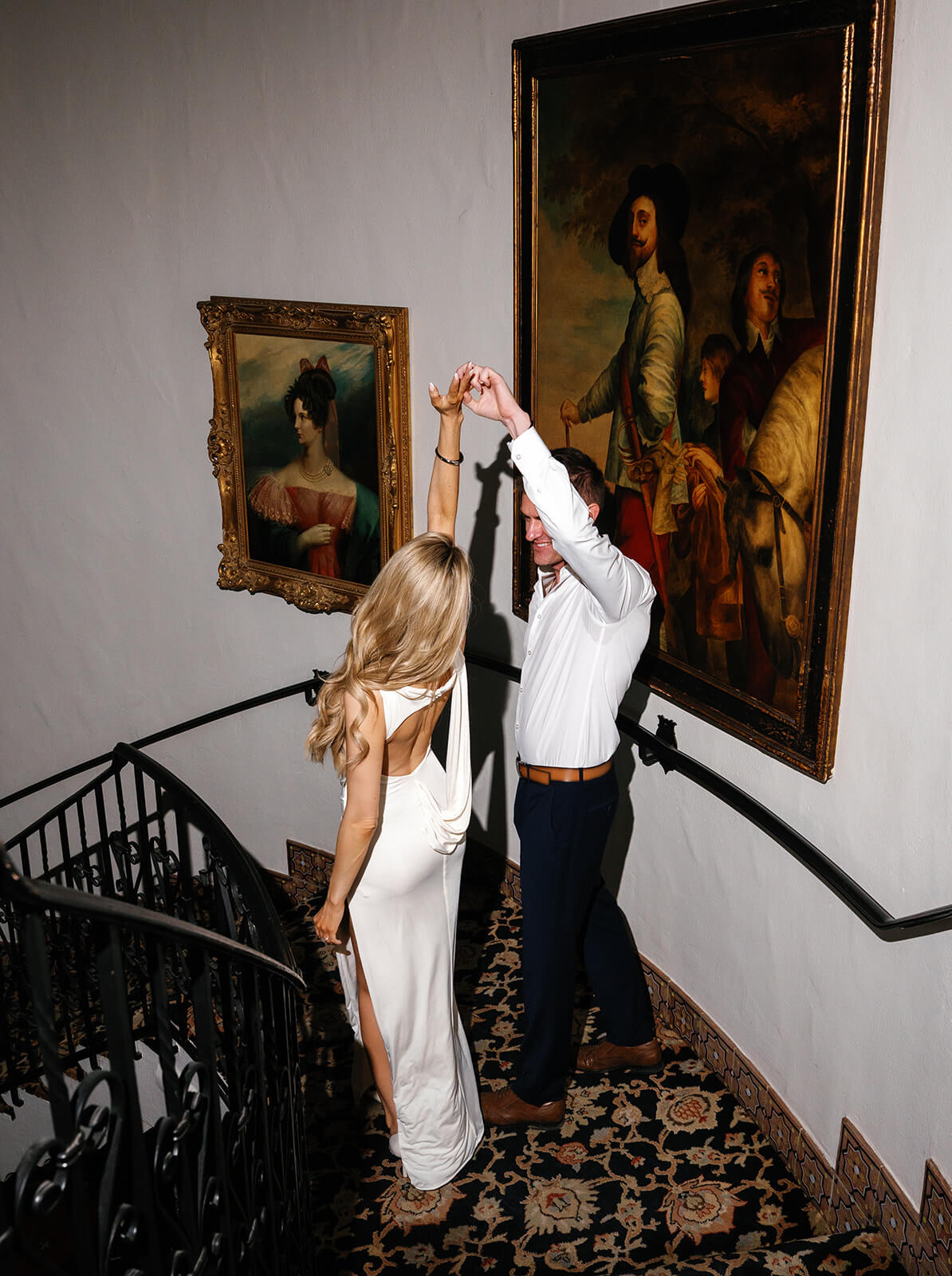 Couple dancing on staircase inside Wrigley Mansion wedding venue with framed vintage artwork and patterned carpet
