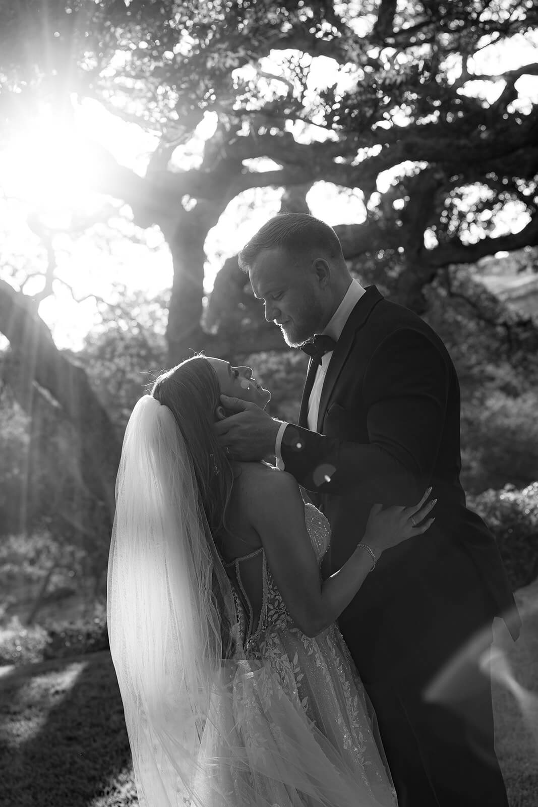 Black and white bridal portrait at a San Luis Obispo wedding venue, featuring a bride and groom embracing under a tree with dramatic sunlight and natural outdoor scenery.