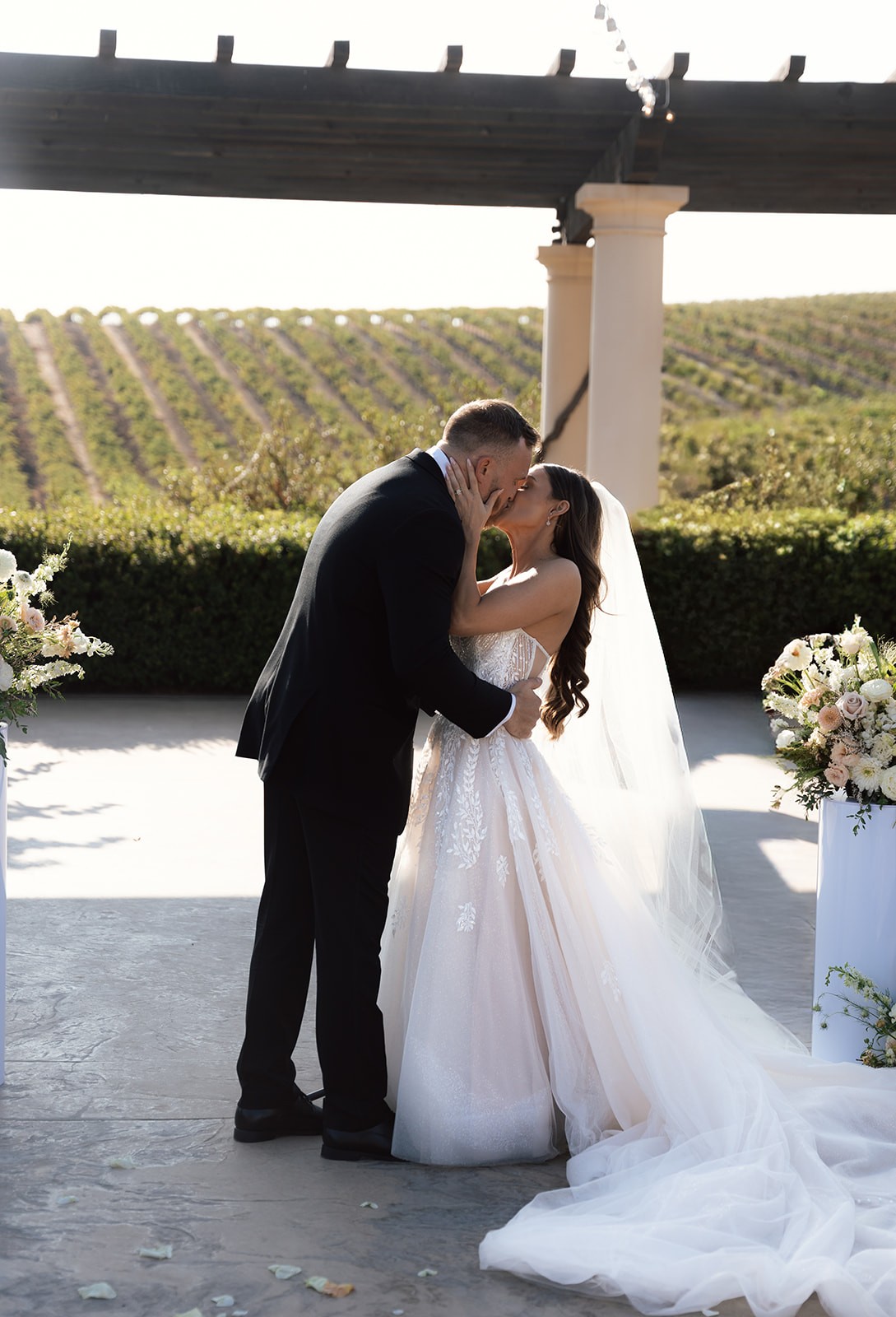 Bride and groom sharing a kiss during an outdoor ceremony at Villa San Juliette, a San Luis Obispo wedding venue with vineyard views and a pergola backdrop