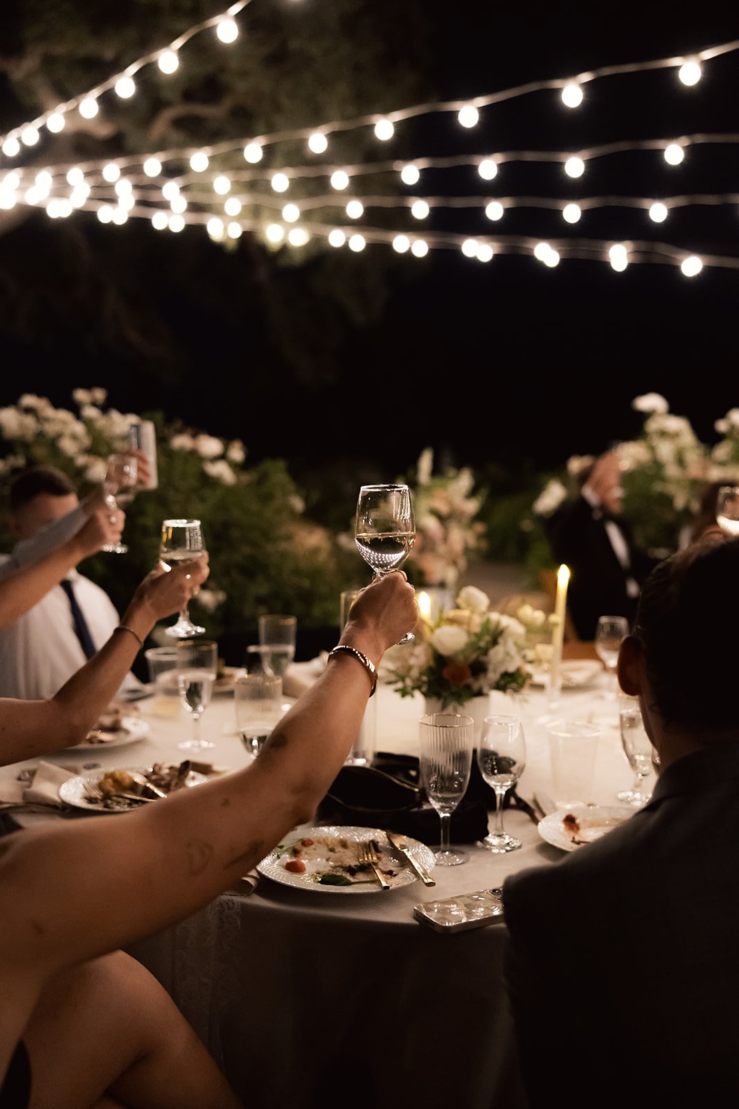 Guests raising glasses during a candlelit outdoor reception at a wedding venue in SLO County with string lights and floral centerpieces at Villa San Juliette