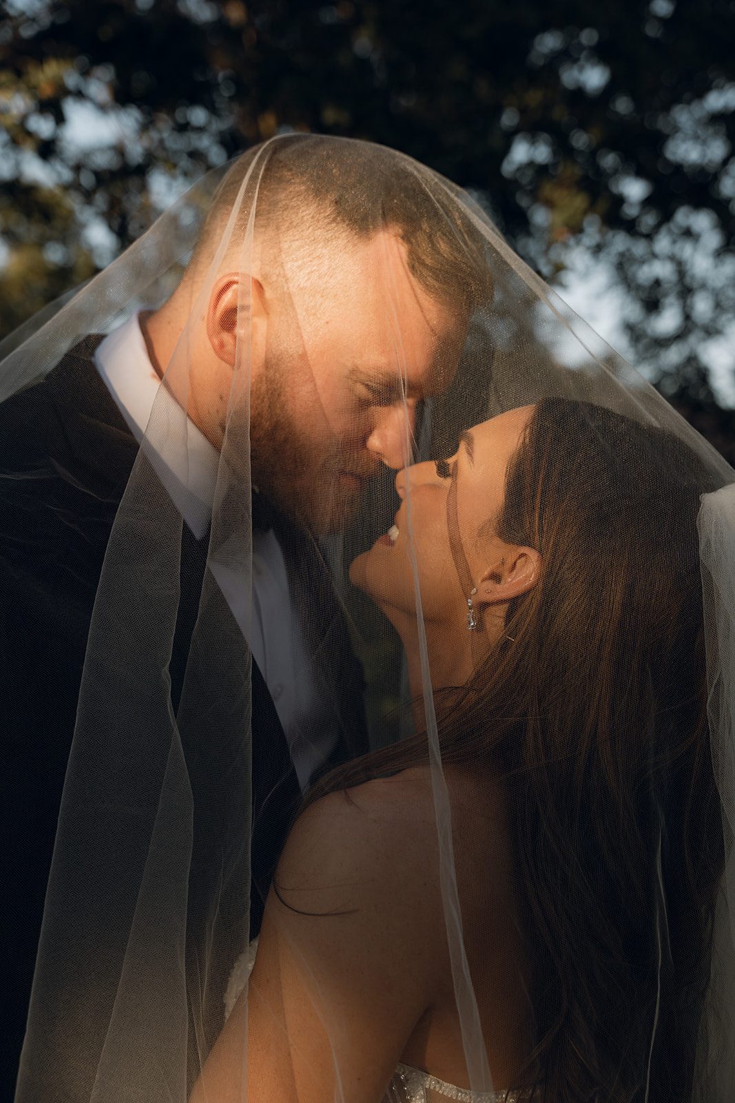 Intimate close-up of bride and groom leaning in toward each other under the bride's flowing veil at an intimate wedding venue in California
