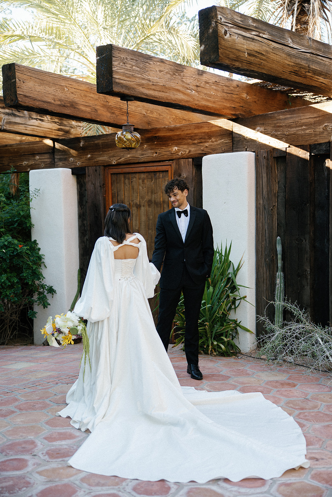 Couple standing beneath wooden pergola in desert courtyard