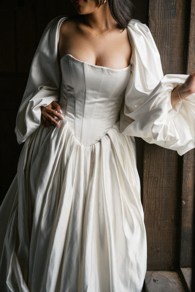 Bride adjusting flowing wedding dress indoors near window light