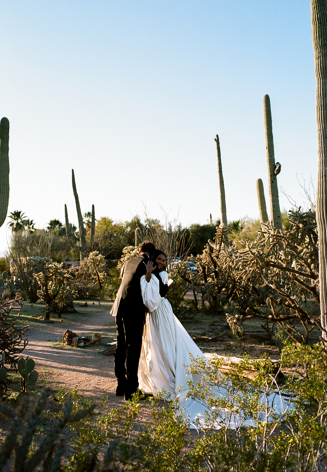 Couple hugs among cacti along sunlit desert path