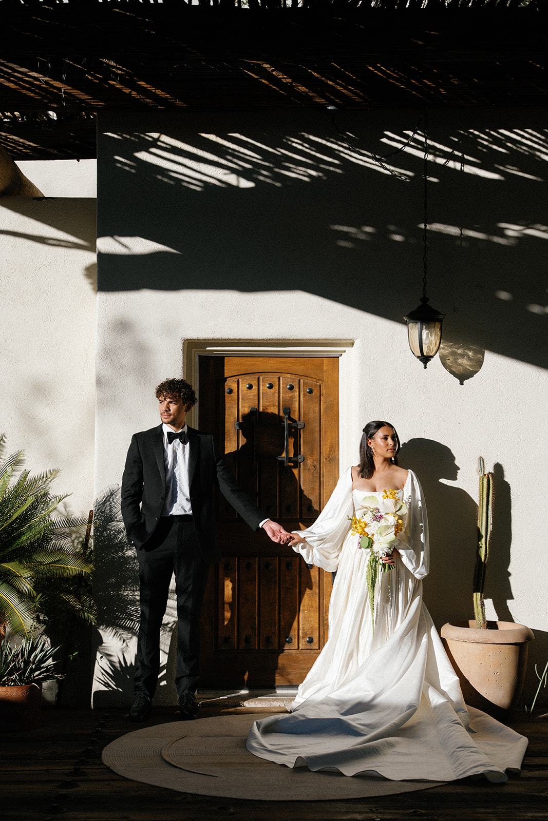 Couple holds hands outside sunlit stucco home