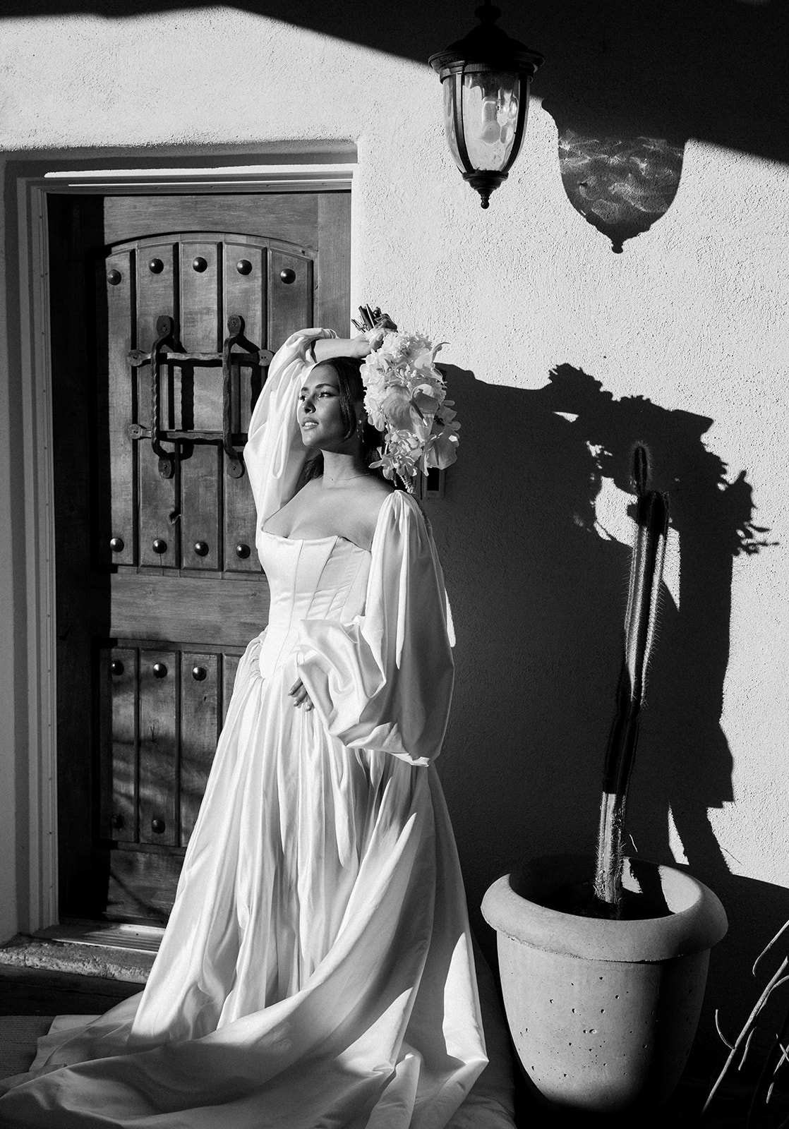 Bride poses in veil beside doorway with dramatic shadow