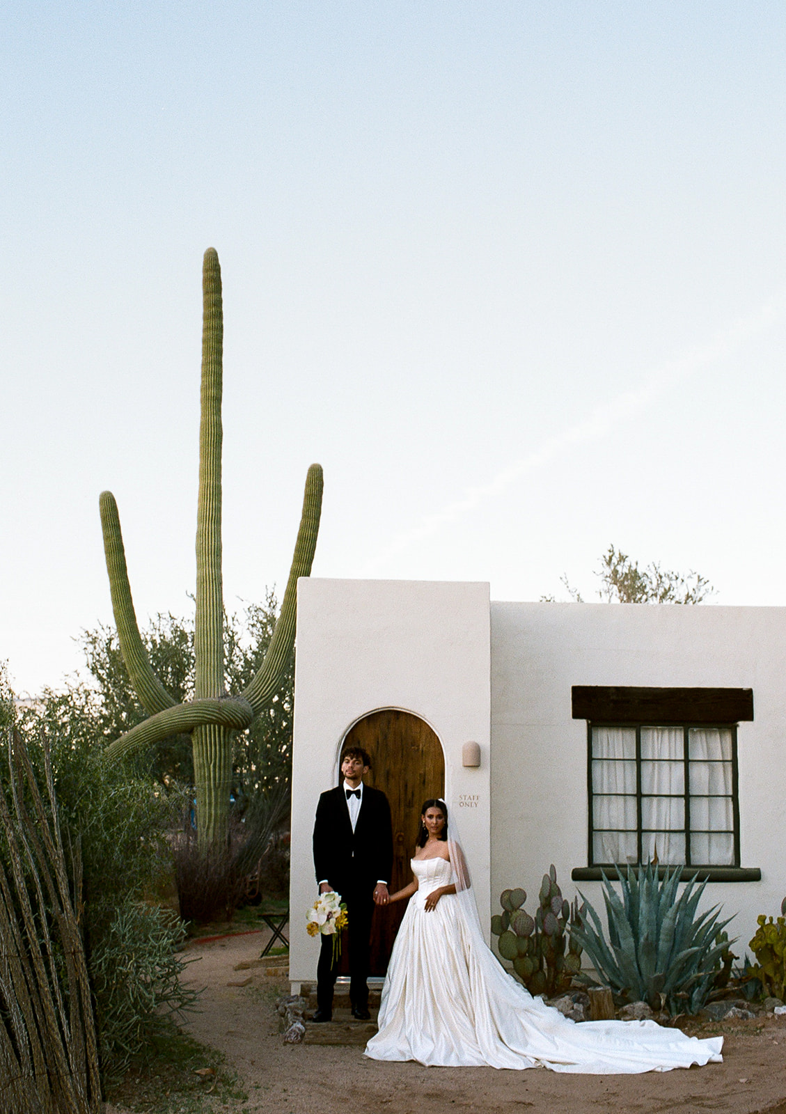 Couple stands near cactus and modern desert home exterior
