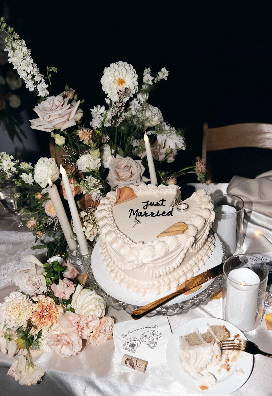 Heart-shaped "Just Married" wedding cake surrounded by tapered candles and blush floral arrangements at an intimate wedding venue in California