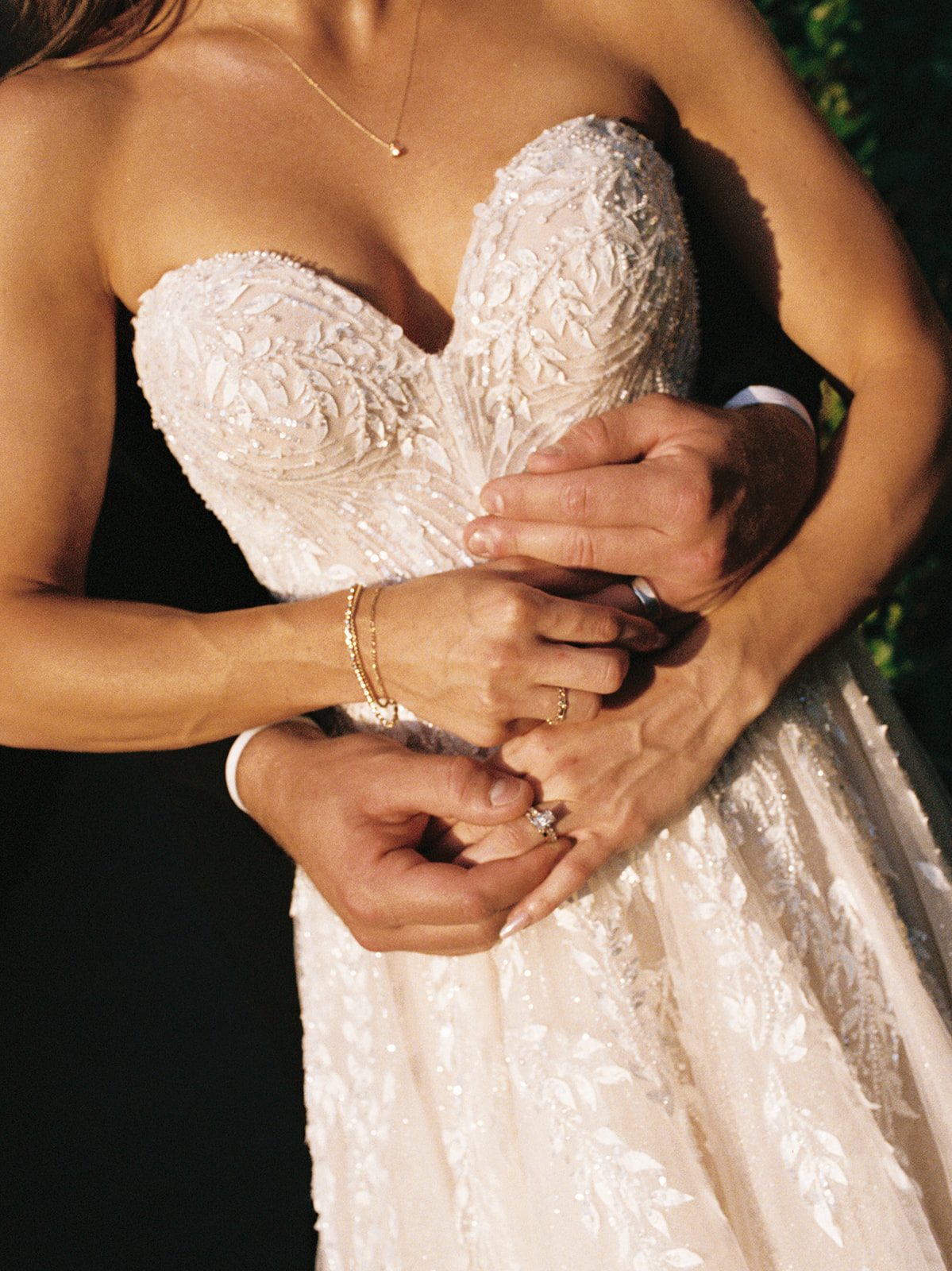 Close-up of a groom's hands embracing his bride's waist, showcasing her engagement ring and wedding band against her beaded strapless gown at Villa San Juliette