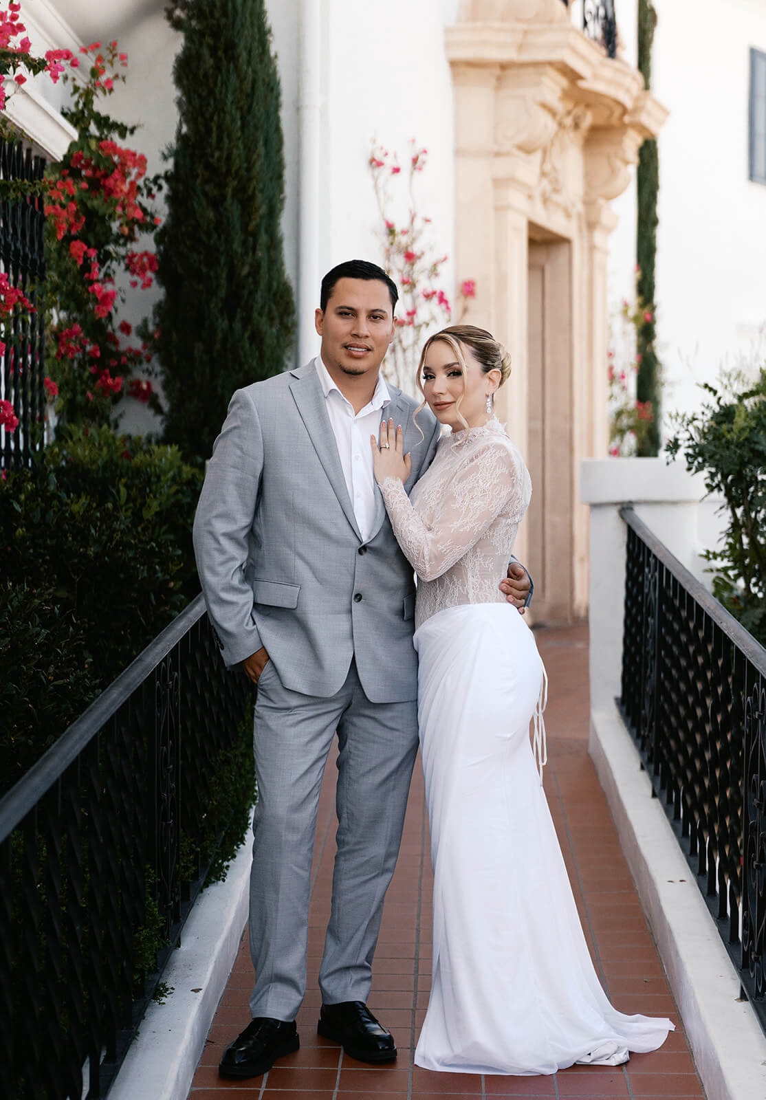 Bride and groom posing together along a walkway at the Wrigley Mansion, an iconic Phoenix Arizona wedding venue with lush greenery and Mediterranean-style details.