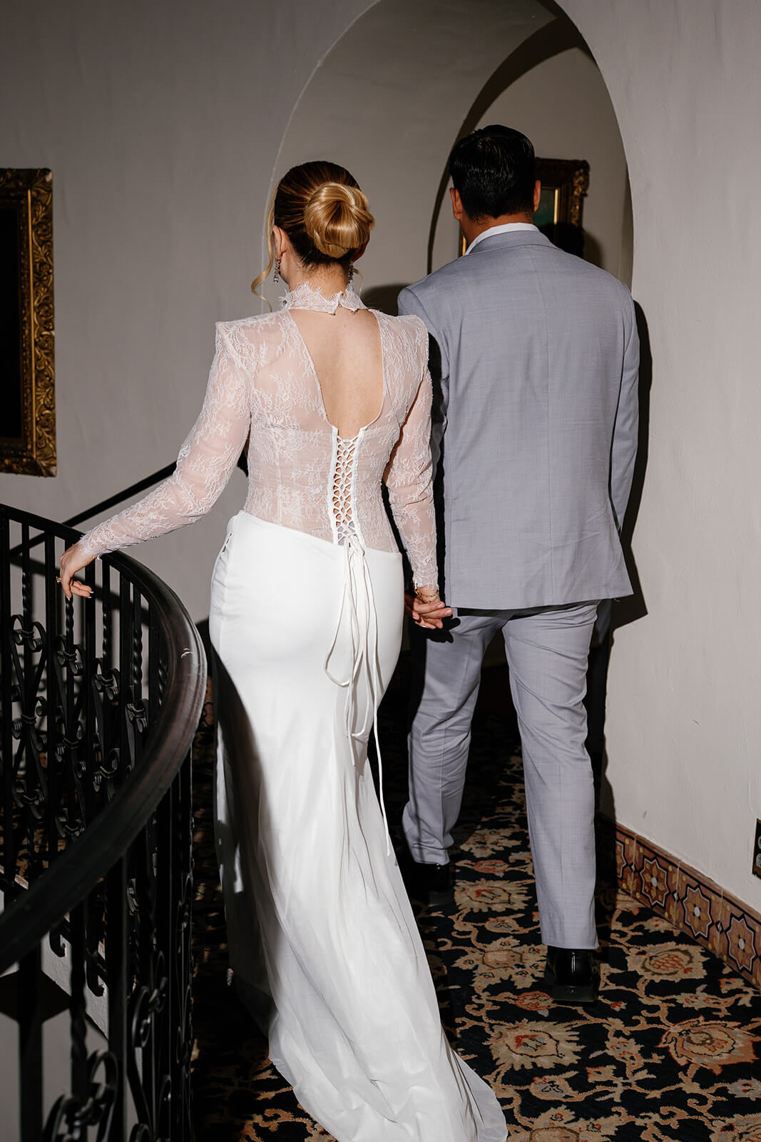 Bride and groom walking hand in hand down a curved hallway with patterned carpet inside the Wrigley Mansion, a unique Arizona wedding venue.