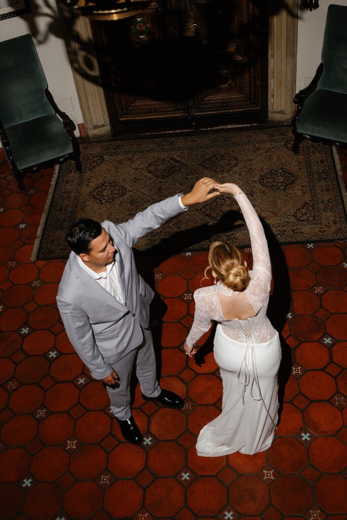 Overhead view of newlyweds dancing together on patterned tile flooring inside an ornate historic venue.