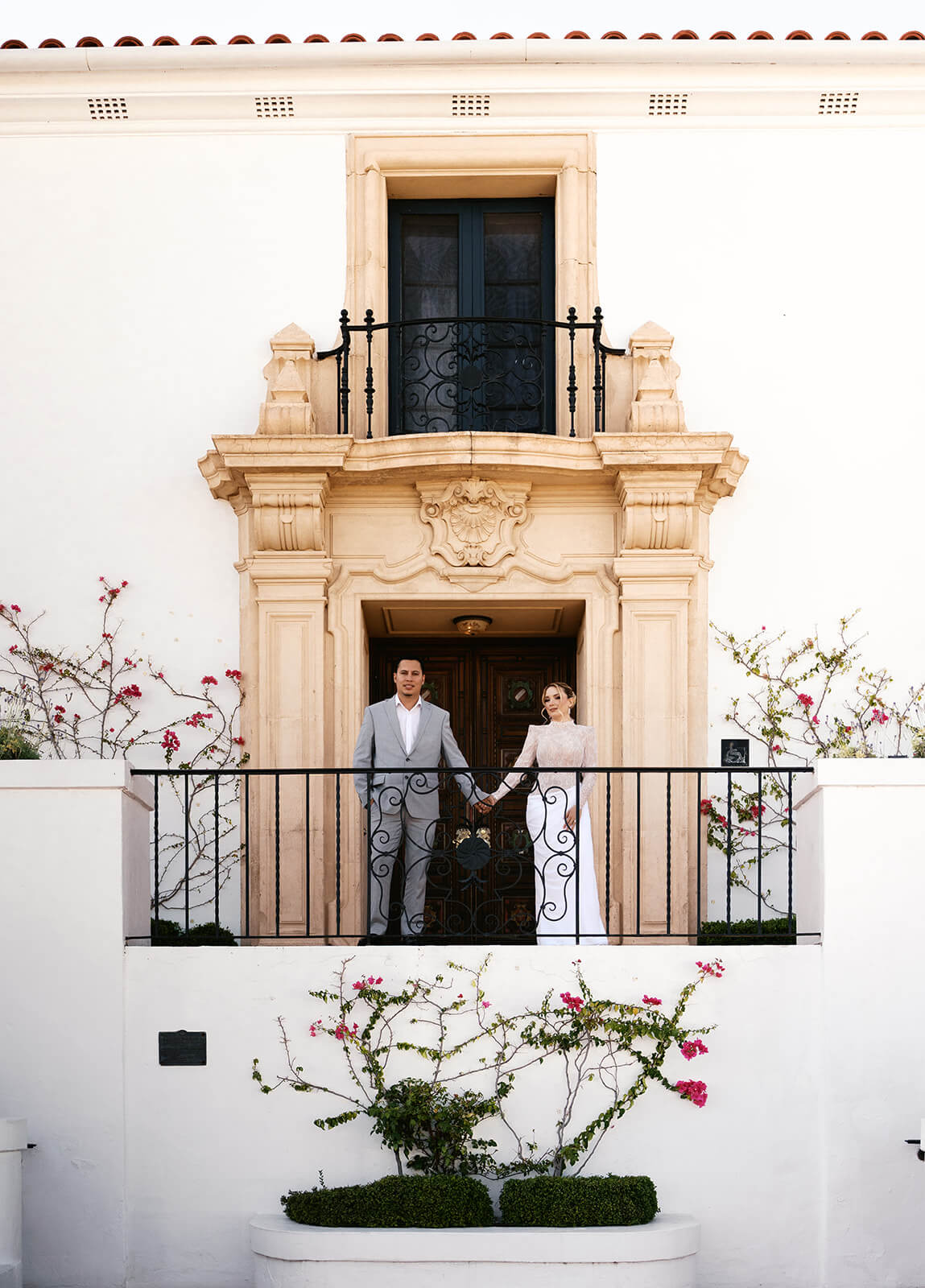 Couple standing on a balcony at the Wrigley Mansion in Phoenix, Arizona, framed by ornate architecture and blooming bougainvillea at an elegant wedding venue.