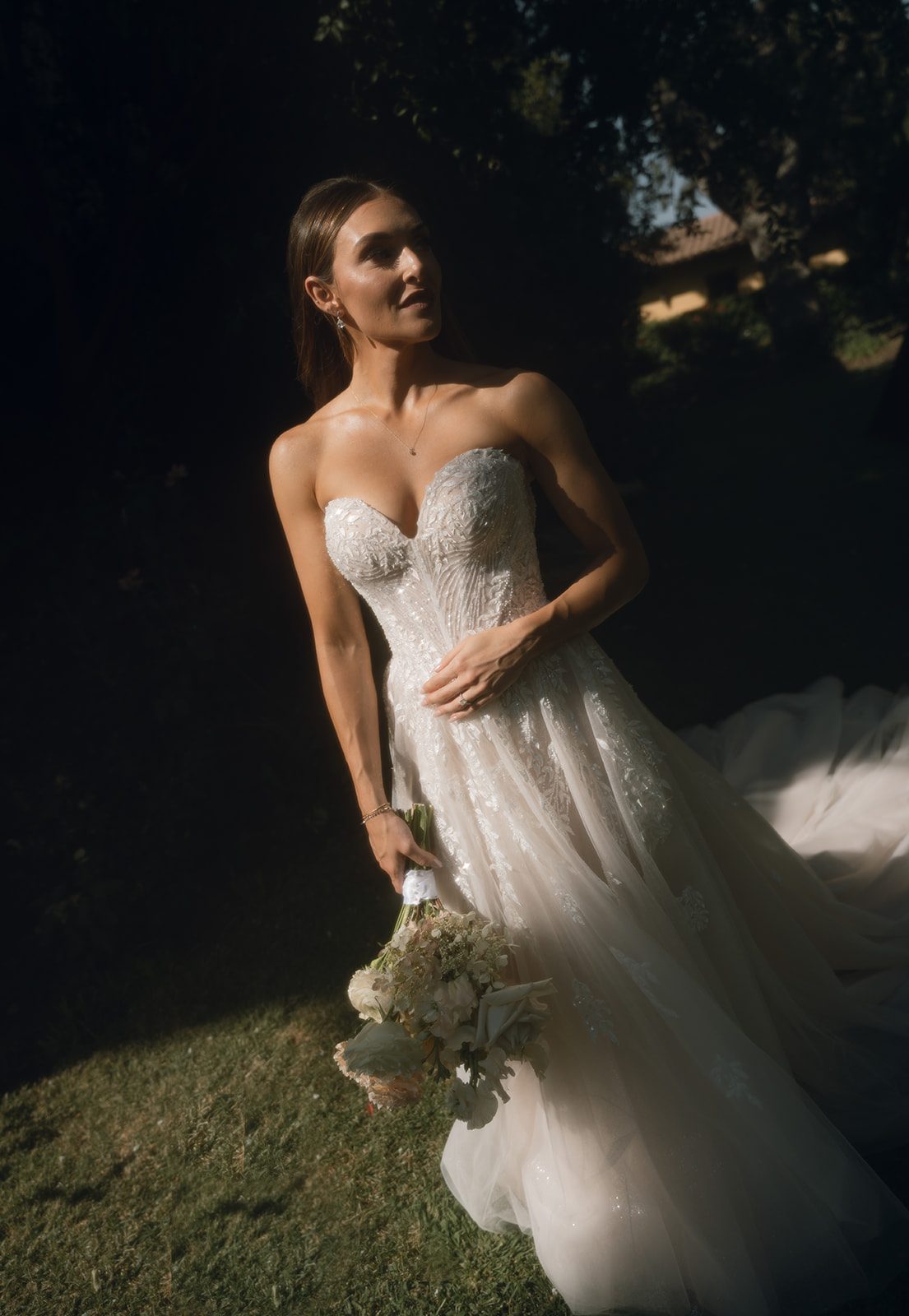 Dramatic editorial bridal portrait with bride in a strapless ballgown holding a bouquet in dappled garden light at a wedding venue in SLO county