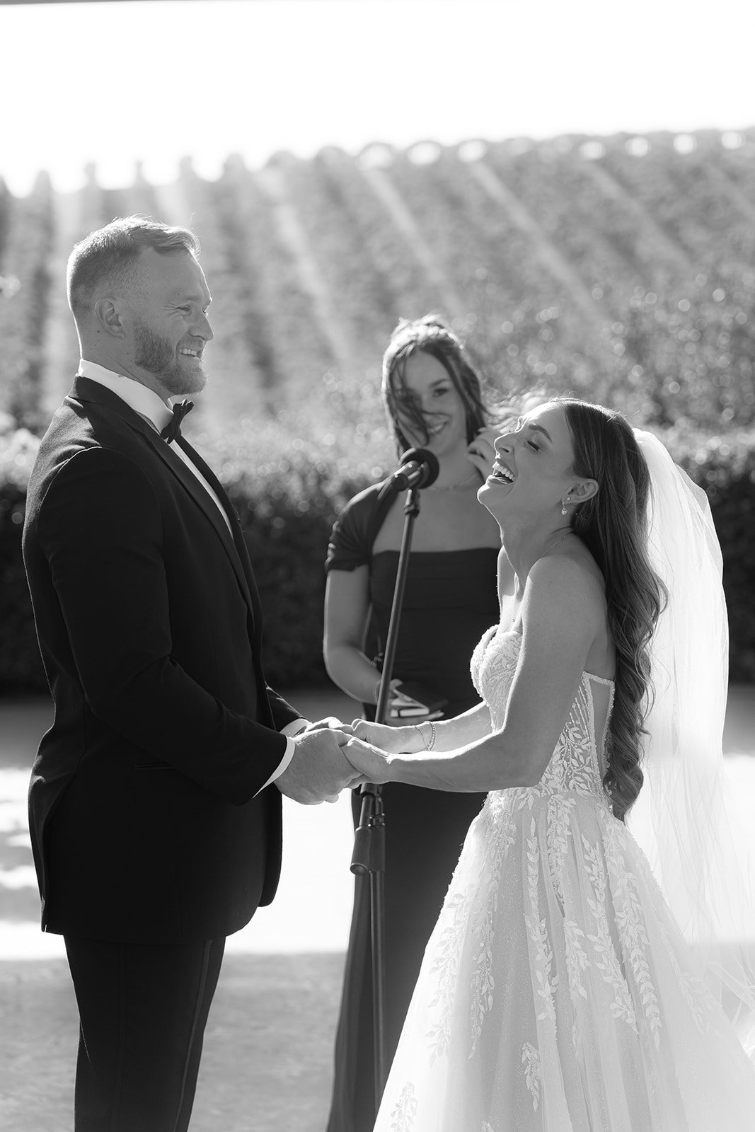 Black and white photo of a bride laughing joyfully while holding hands with her groom at the altar during an SLO wedding ceremony