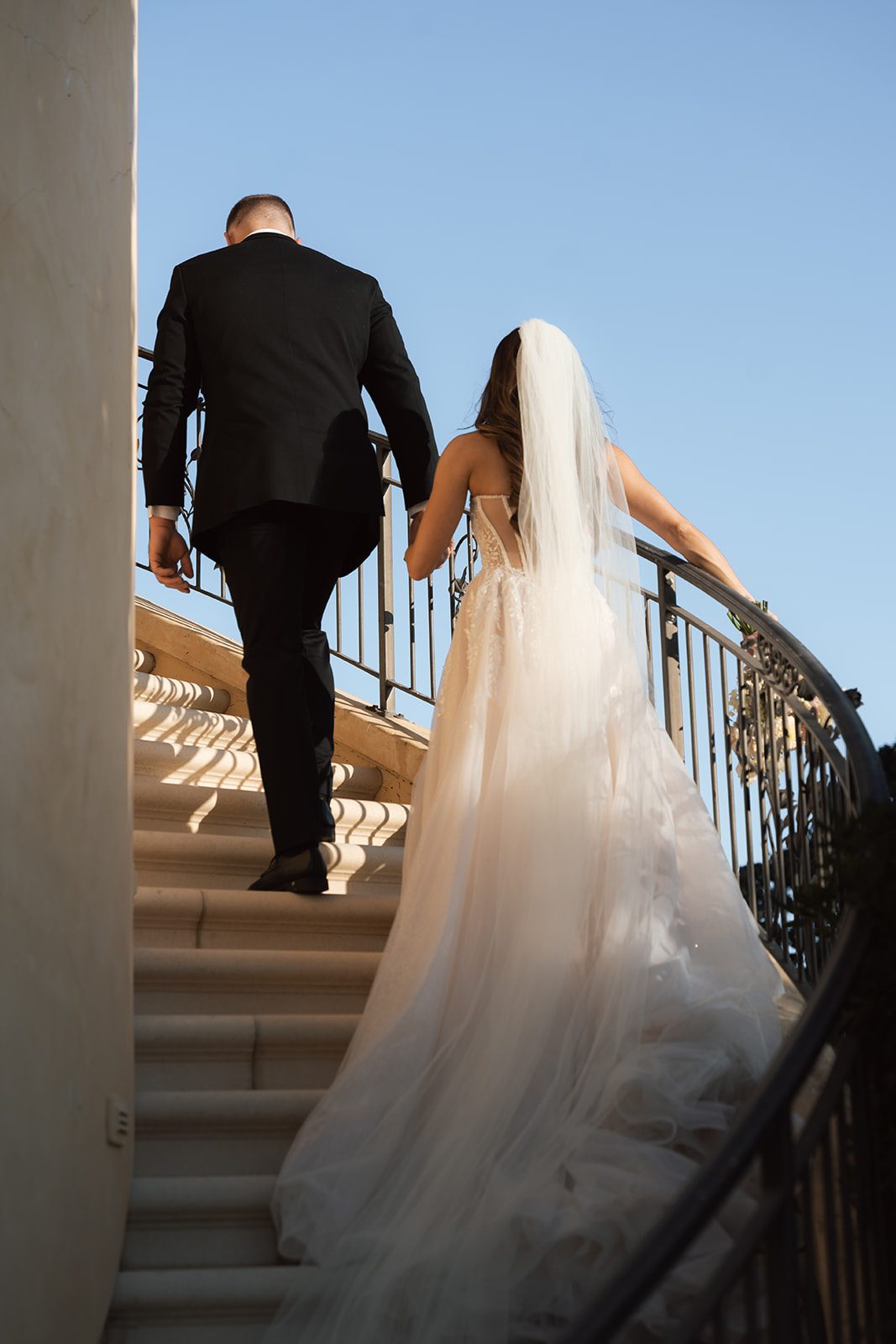 Bride and groom climbing the spiral staircase hand in hand against a bright blue sky at a wedding venue in SLO county