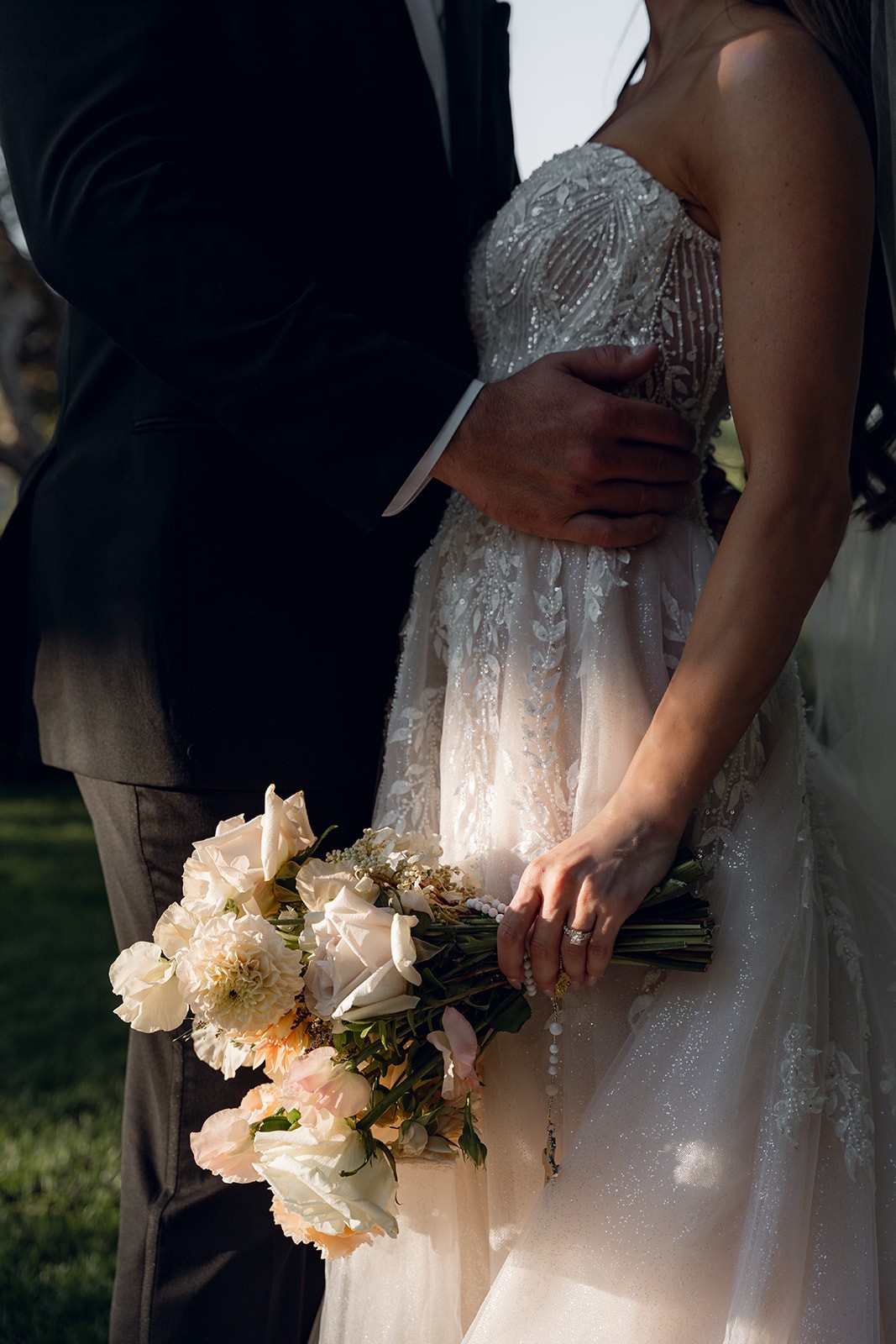 Close-up detail of a bride holding her blush and ivory bouquet against her beaded gown while the groom's hand rests on her waist at Villa San Juliette