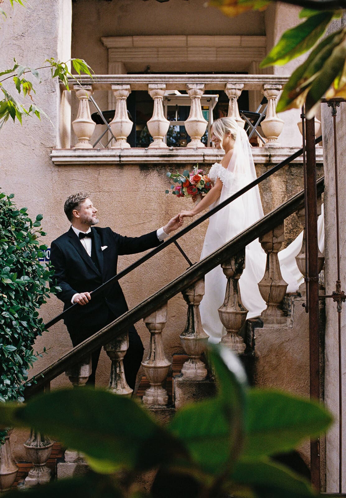 Bride and groom standing together on a staircase surrounded by Spanish-style architecture and greenery during a micro wedding at Tlaquepaque.