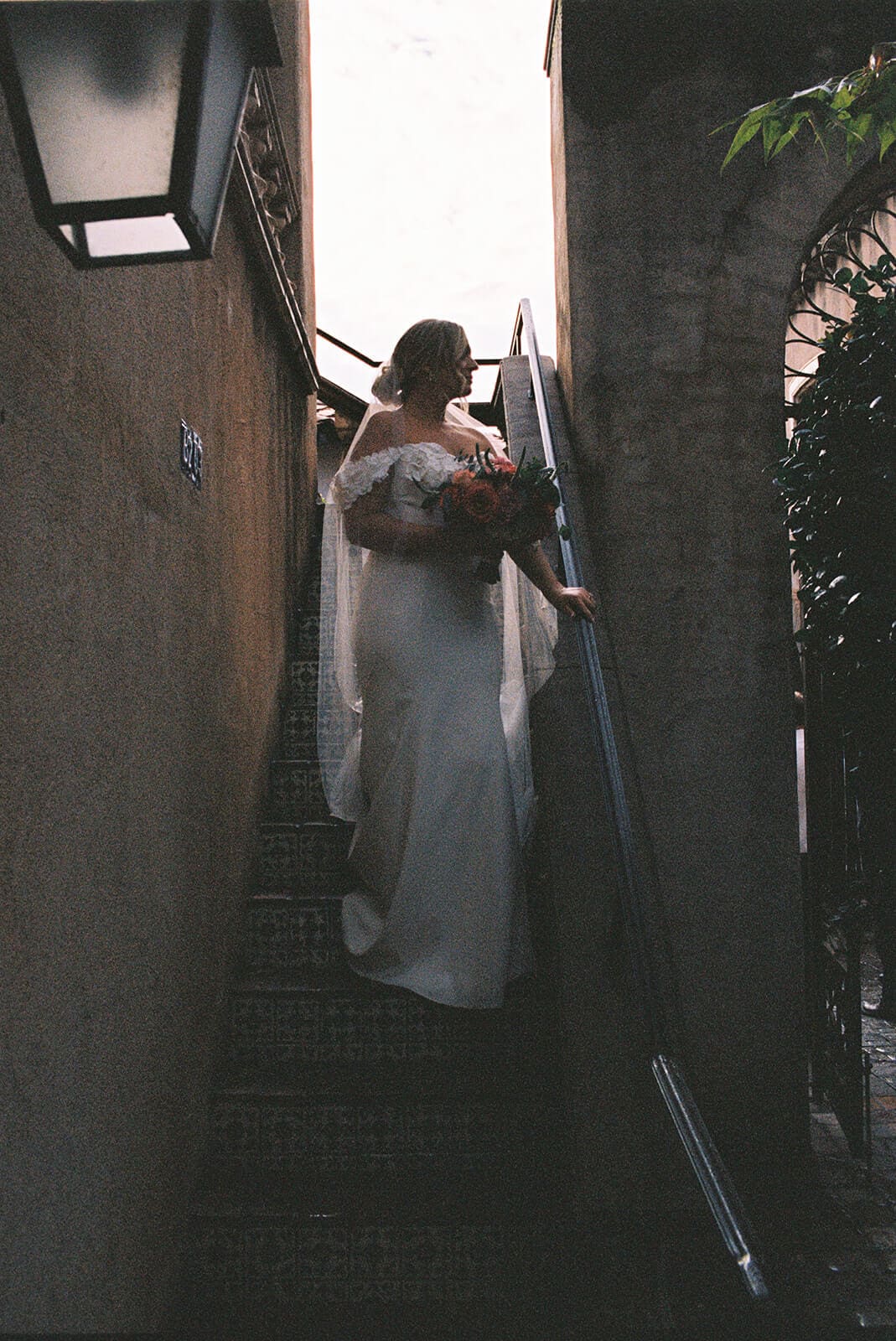 Bride walking up a narrow staircase beside a stucco wall during a micro wedding at Tlaquepaque.