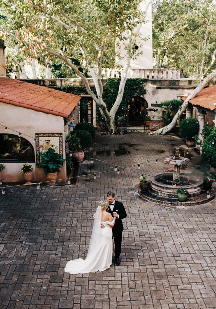 Overhead view of newlyweds embracing in a brick courtyard surrounded by trees and historic architecture.