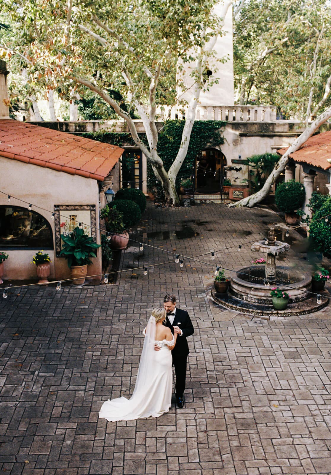 Bride and groom embracing in the center of a brick courtyard surrounded by Spanish-style architecture and greenery during a micro wedding at Tlaquepaque.